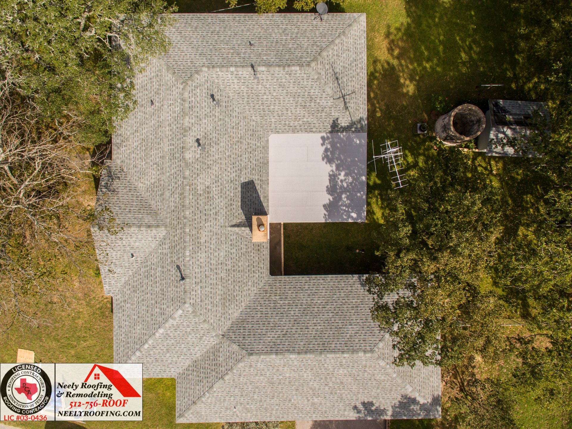 Aerial view of a house with a gray roof, trees around it, and two small logos in the lower left corner