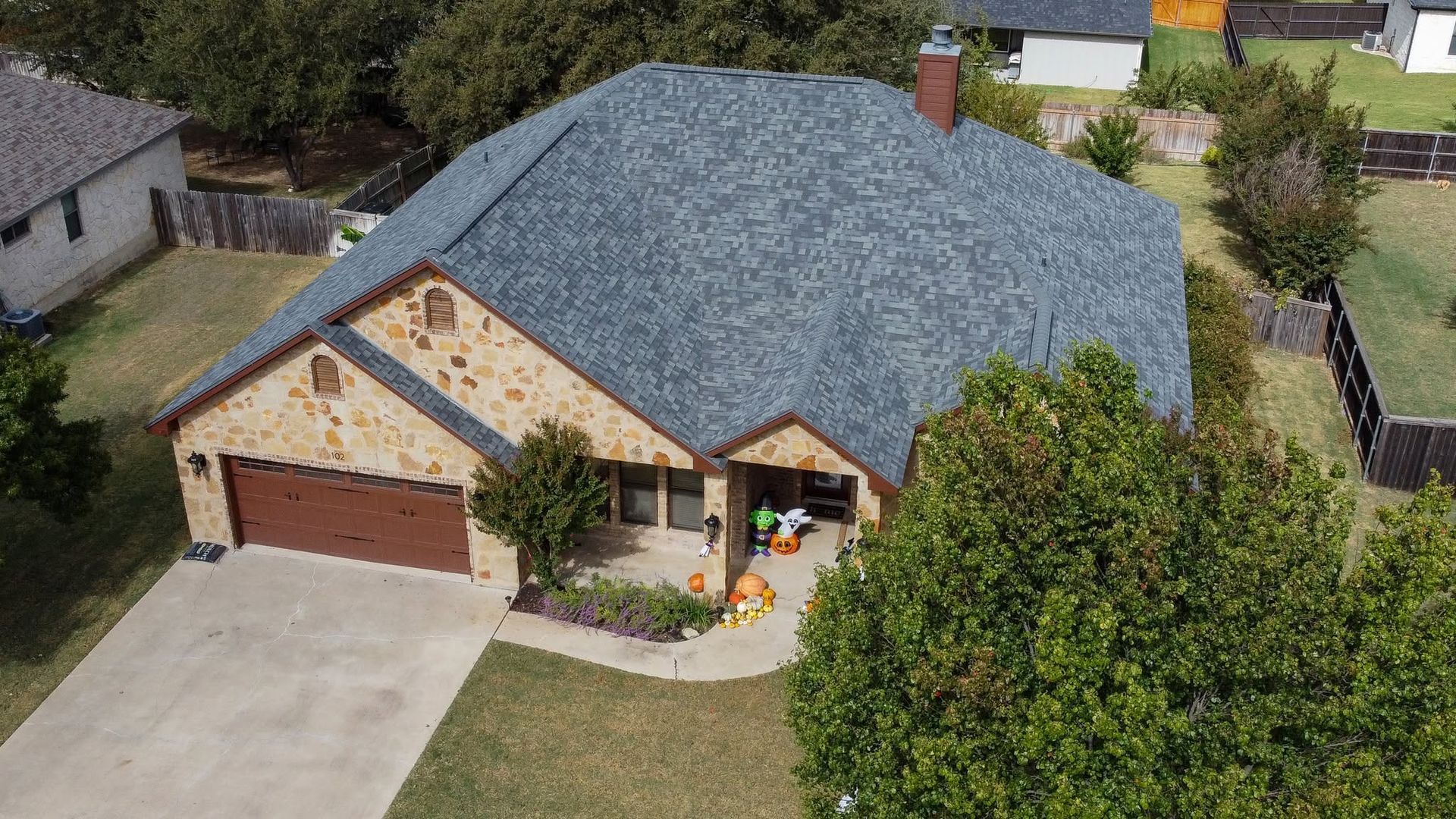 Aerial view of a brick suburban house with a gray roof, driveway, and front yard