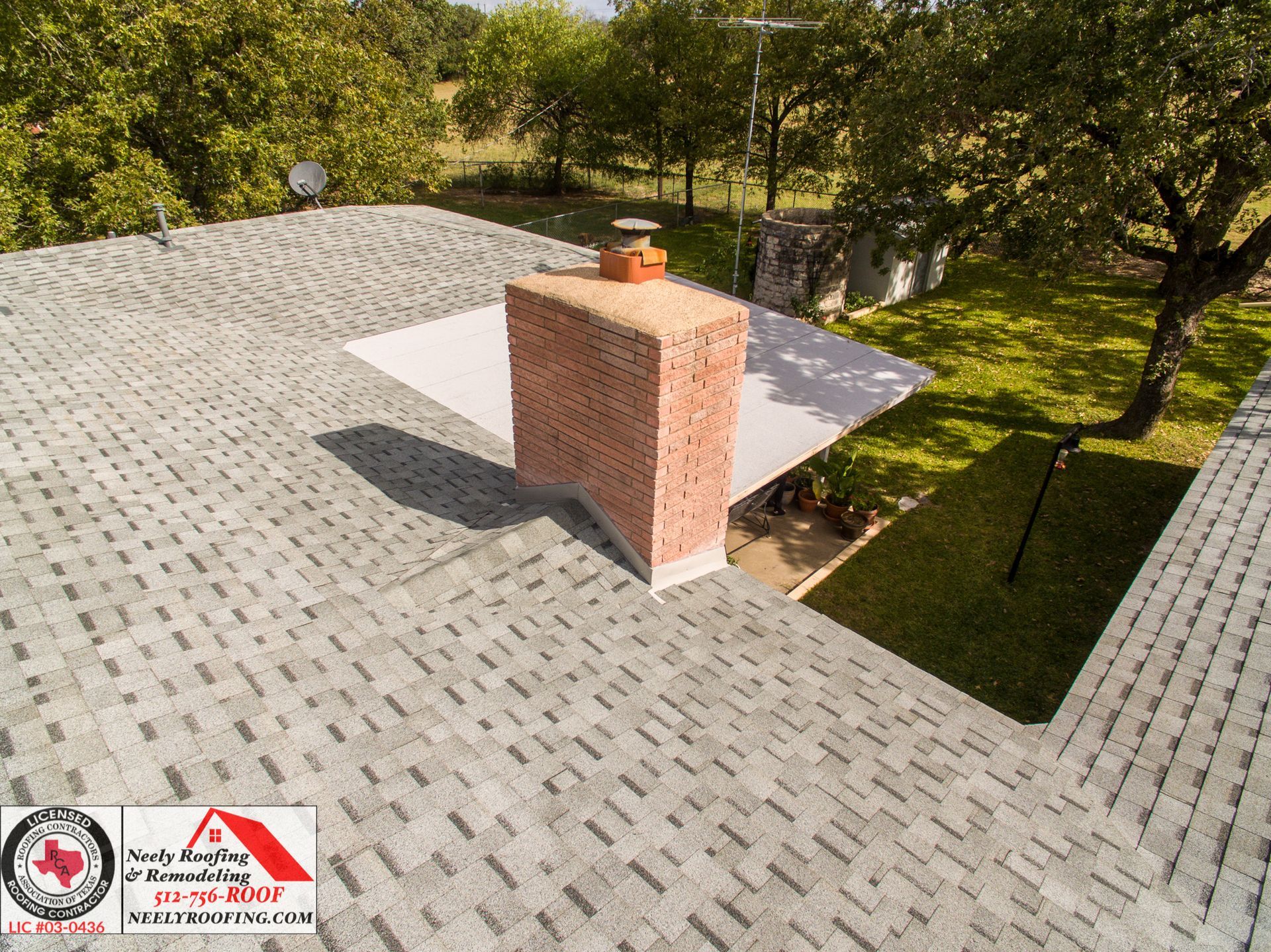 Roof with gray shingles and brick chimney beside a grassy yard and trees