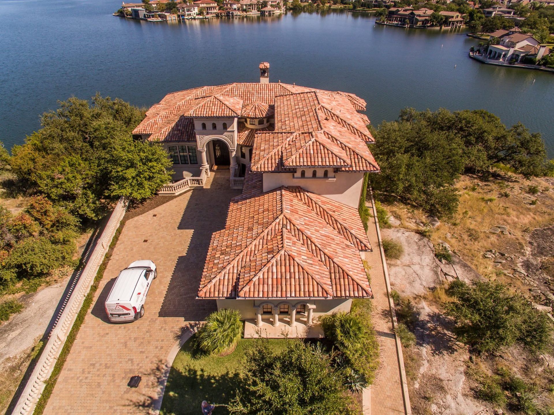 Aerial view of a terracotta-roofed house beside water, with trees and a parked white car