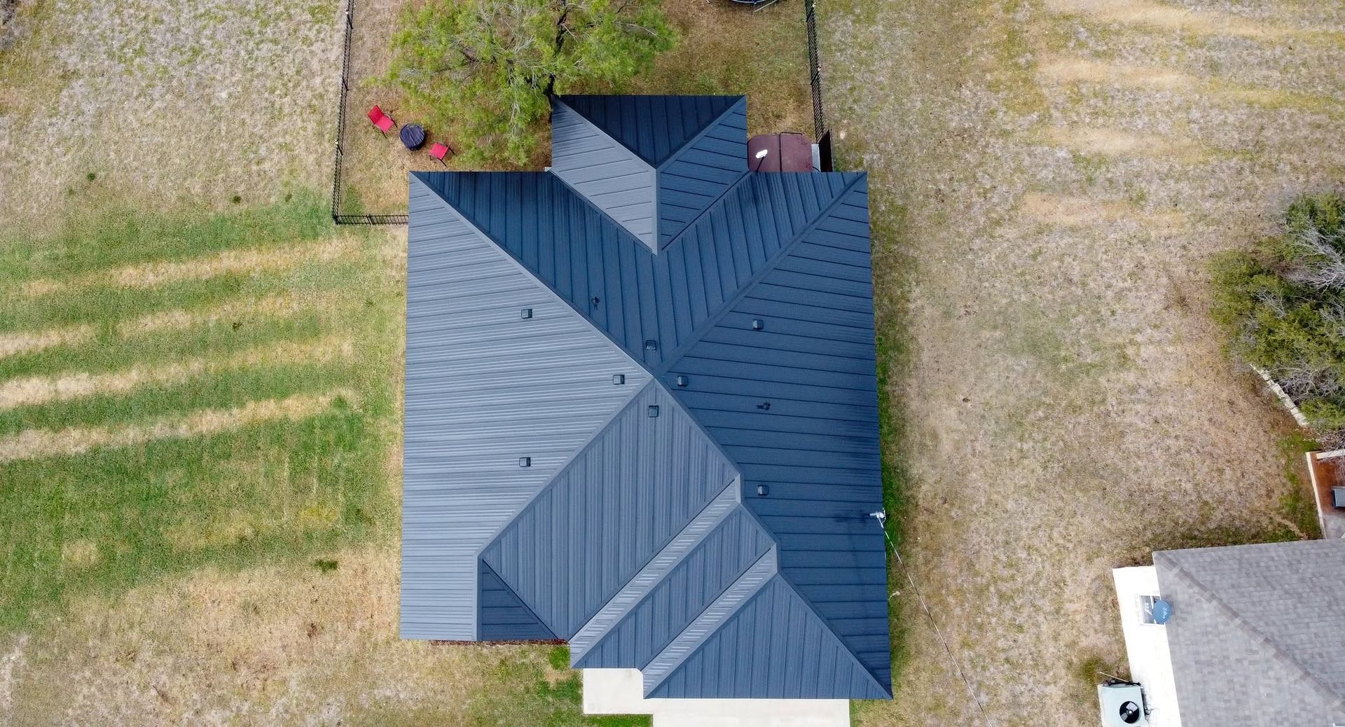 Aerial view of a blue-roofed house surrounded by grassy yard and a driveway.