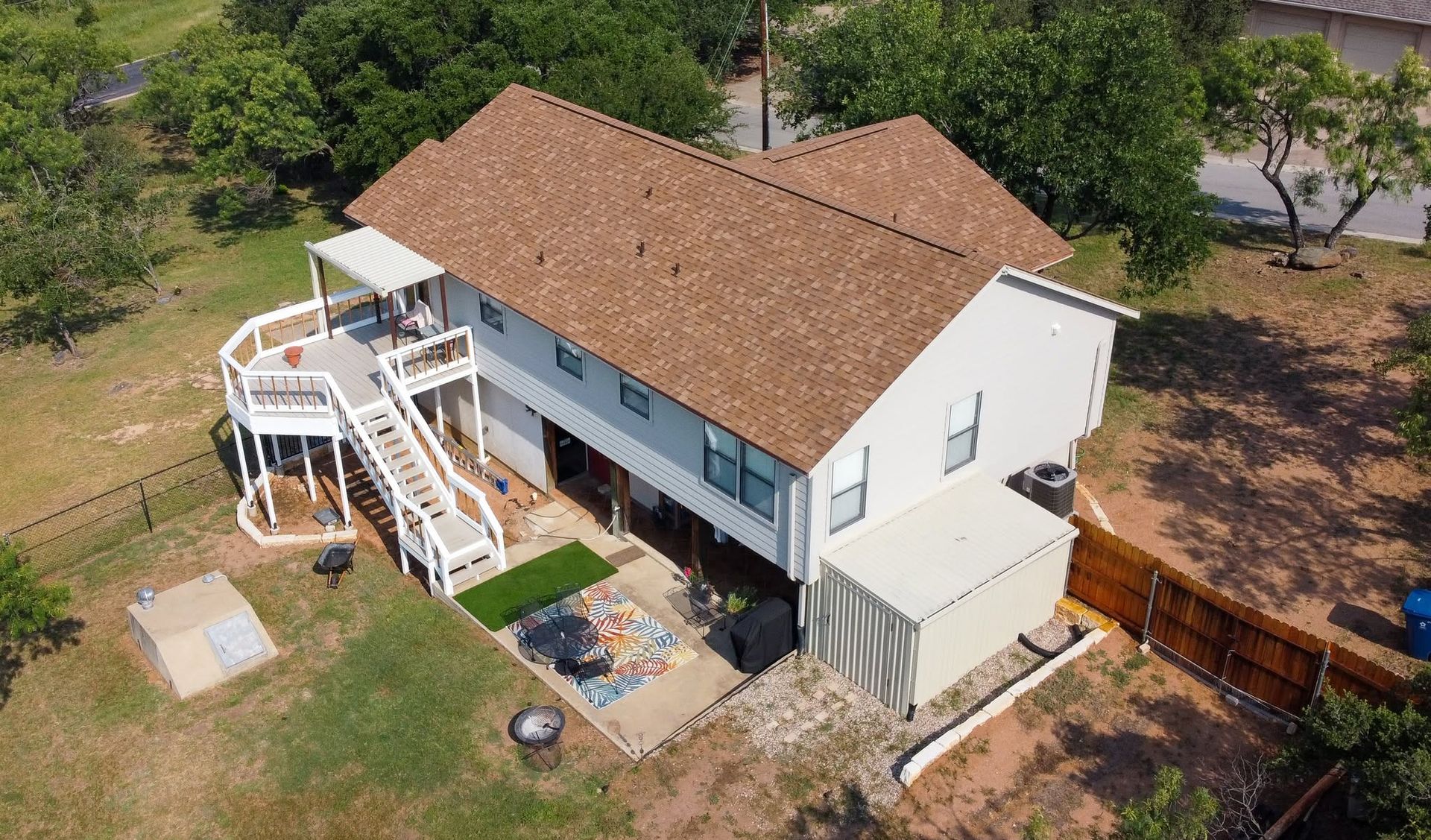 Aerial view of a white house with a brown roof, wraparound deck, and trees in the yard.