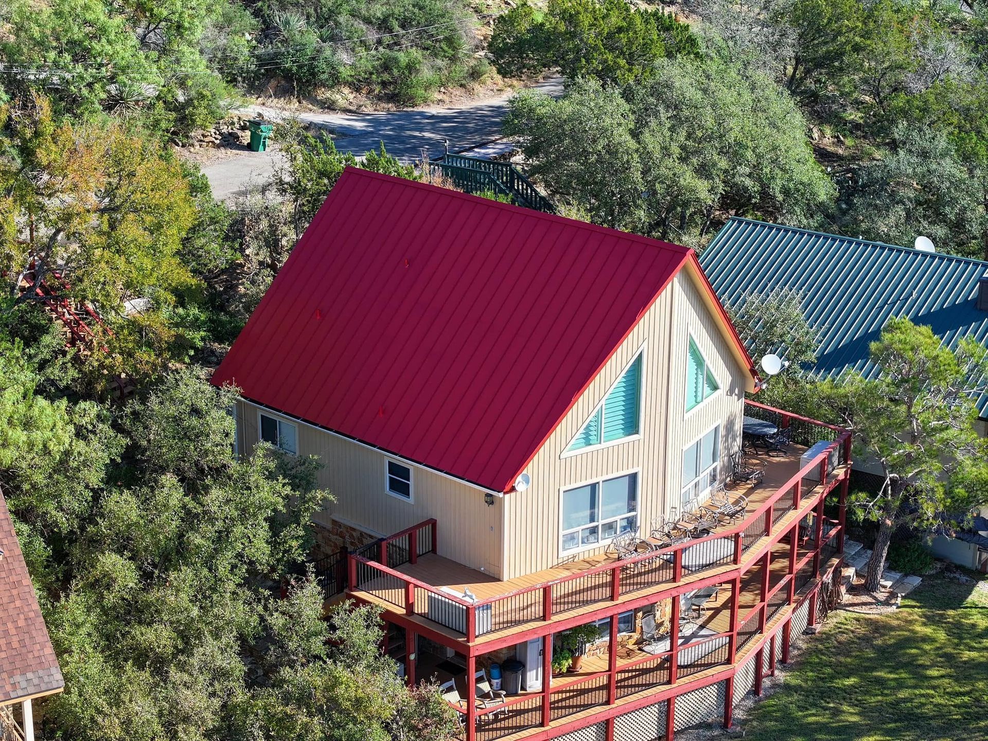 A small house with a red roof and wraparound deck surrounded by trees