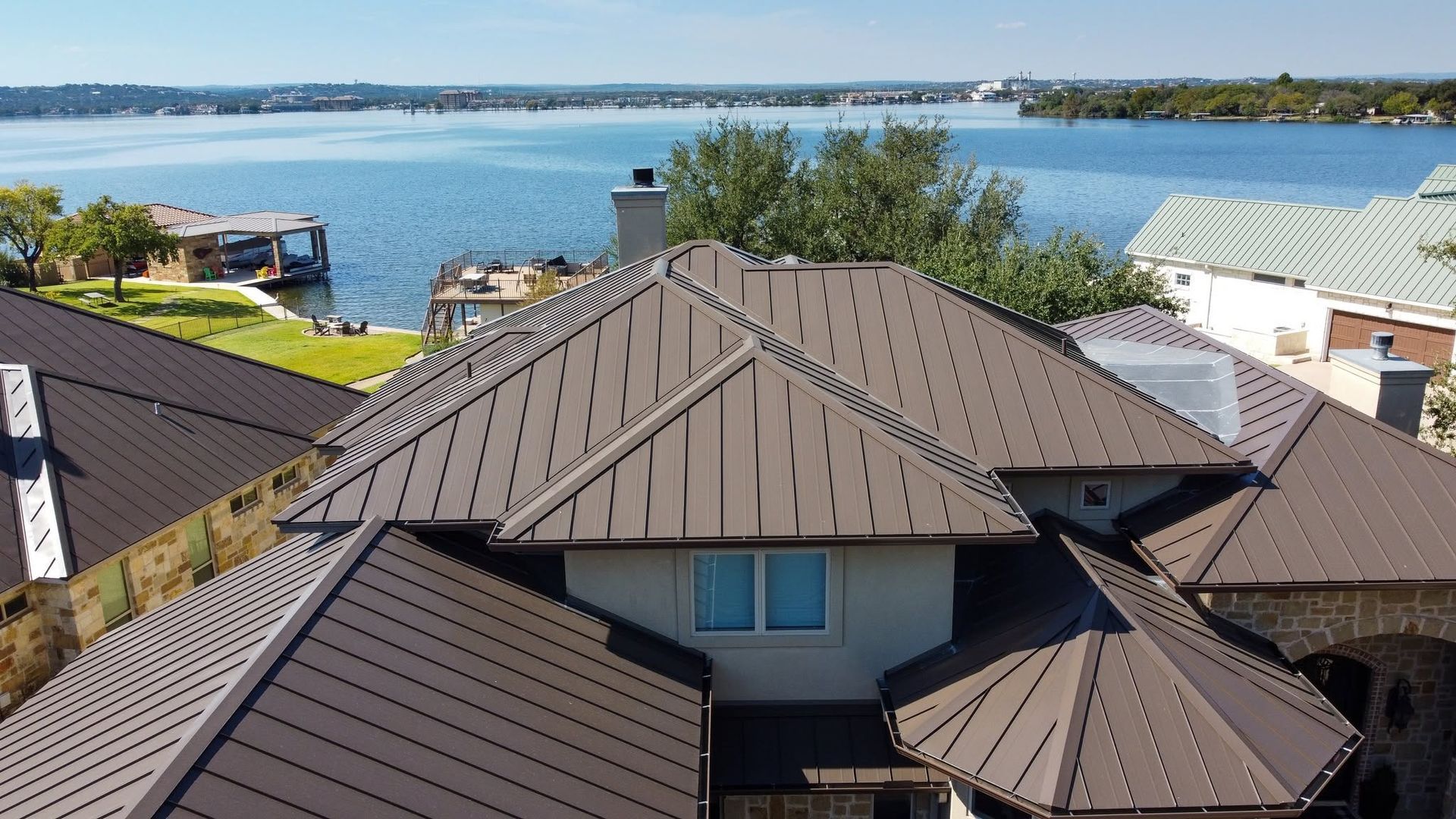 Houses with dark roofs overlook a bright blue waterfront and distant shoreline
