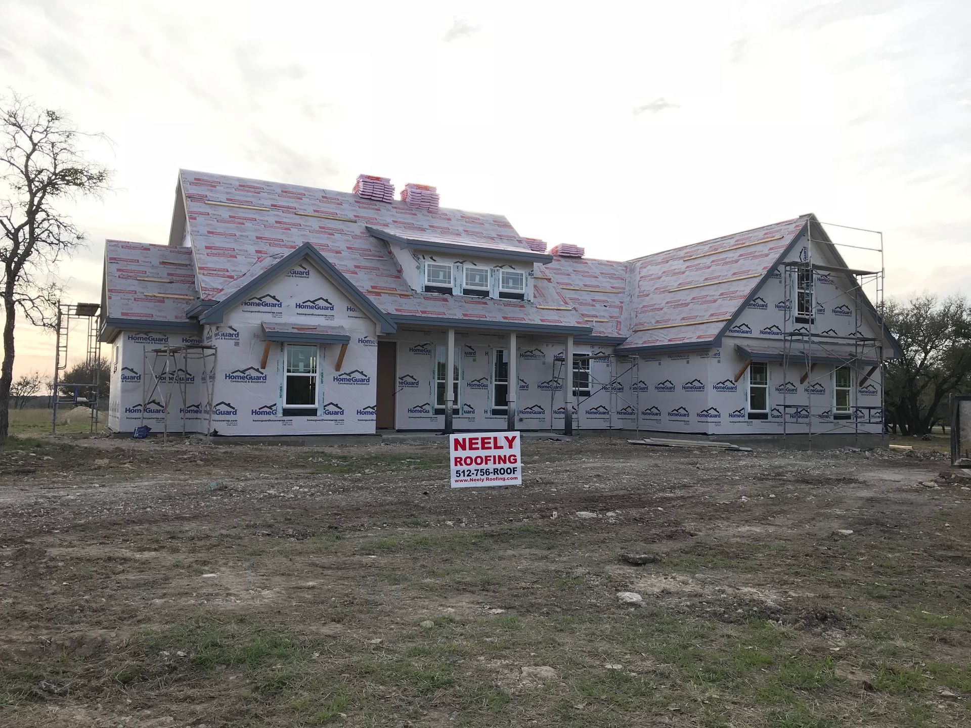 Partially built house with roof shingles and a front yard, with a real estate sign in front