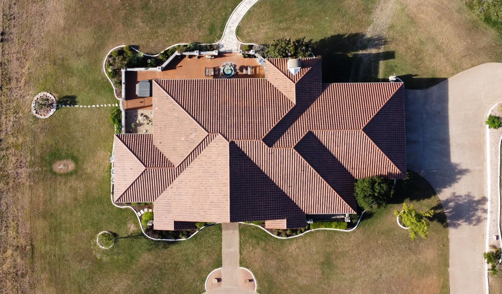Aerial view of a brown-roofed house with a front walkway, lawn, and trees surrounding it.