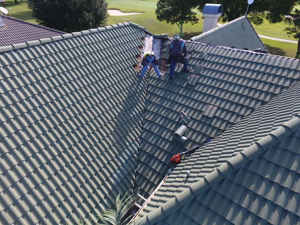 Workers on a gray tiled roof, with a ladder and tools, likely doing roof repairs.