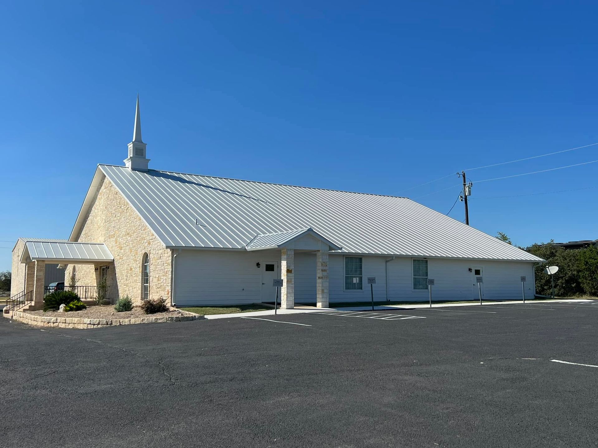 White church building with a small steeple and parking lot under a clear blue sky