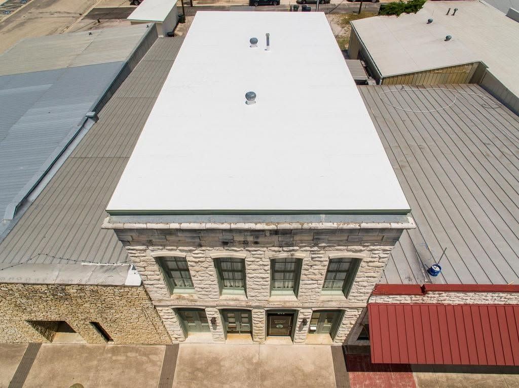 Aerial view of a stone building with a flat white roof and red awning in a courtyard.