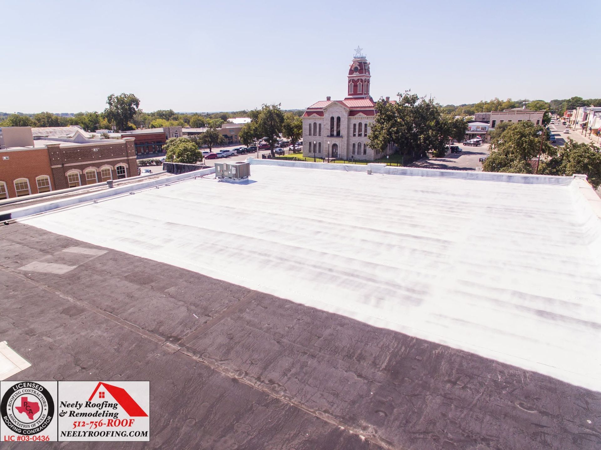 Rooftop with white coated surface and a church tower in the background under a clear sky.