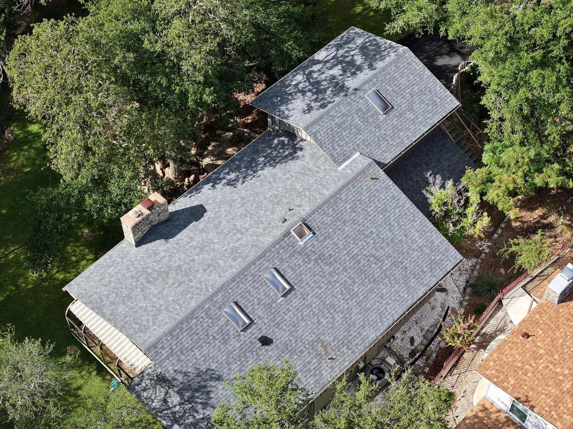 Aerial view of a gray-shingled house surrounded by trees and greenery.