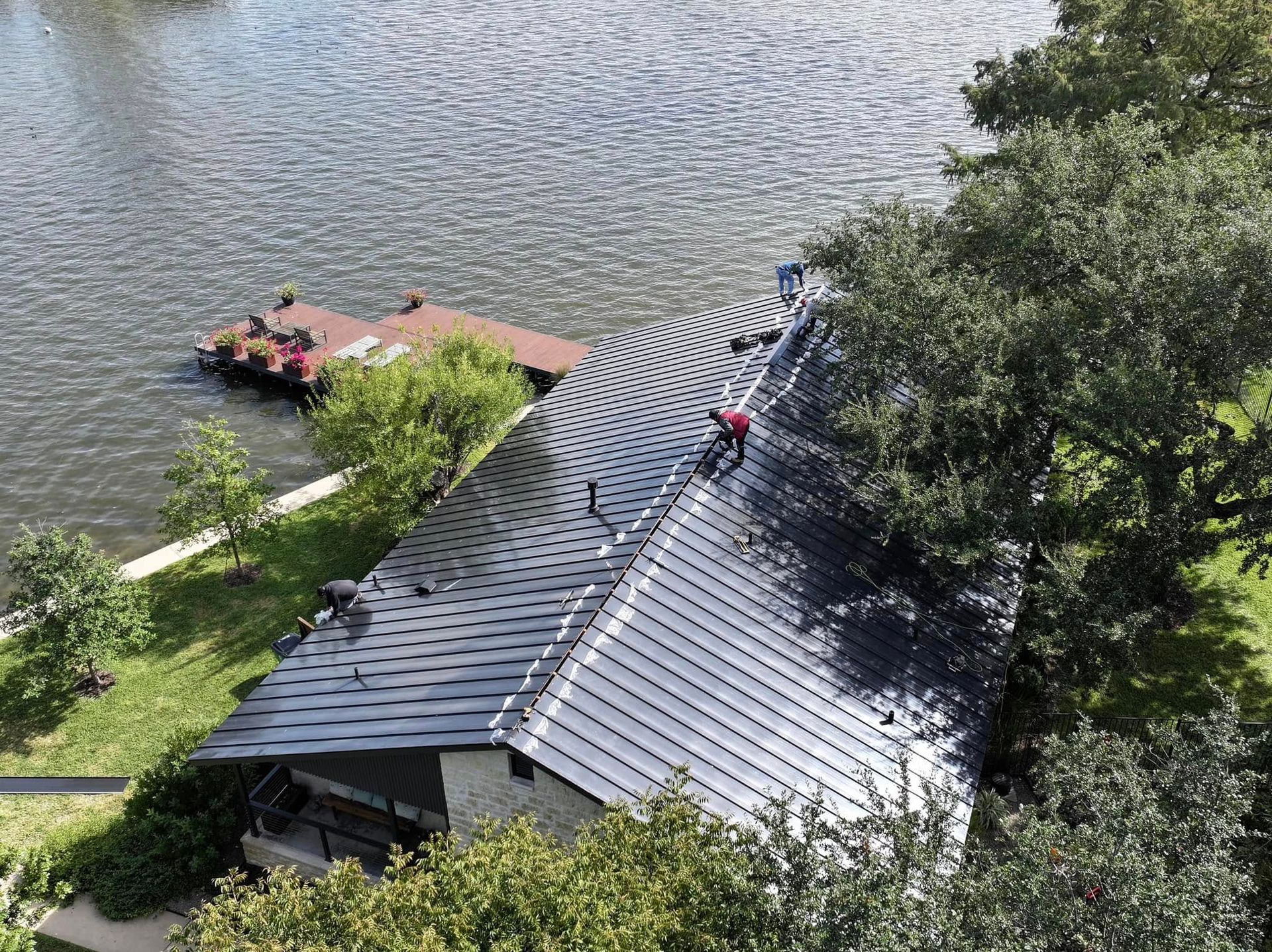 Aerial view of people on a curved gray-roofed building beside a lake and dock.