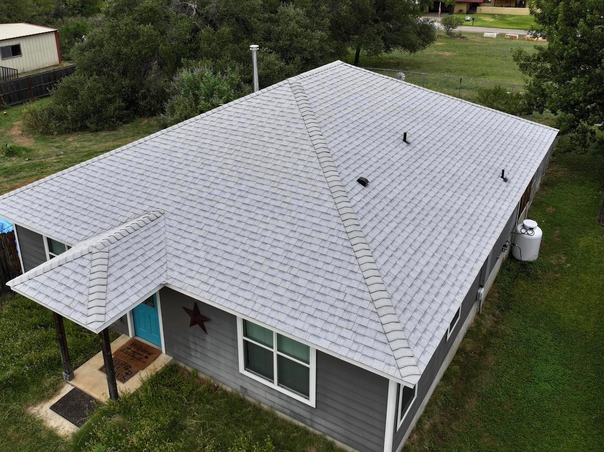 Aerial view of a gray shingle-roofed house with a small front porch and green lawn.