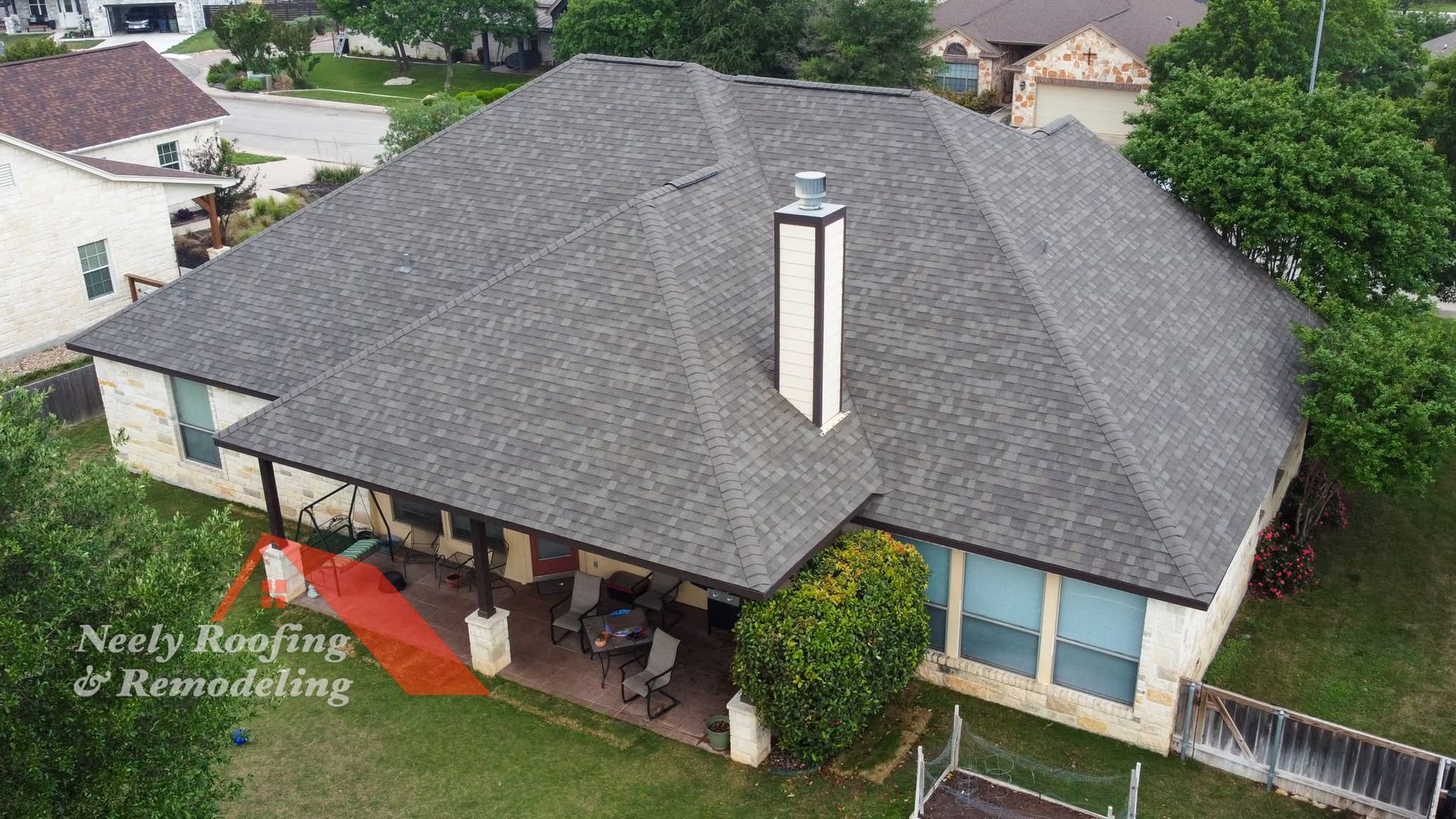 Aerial view of a gray-roofed suburban house with a covered patio and chimney.