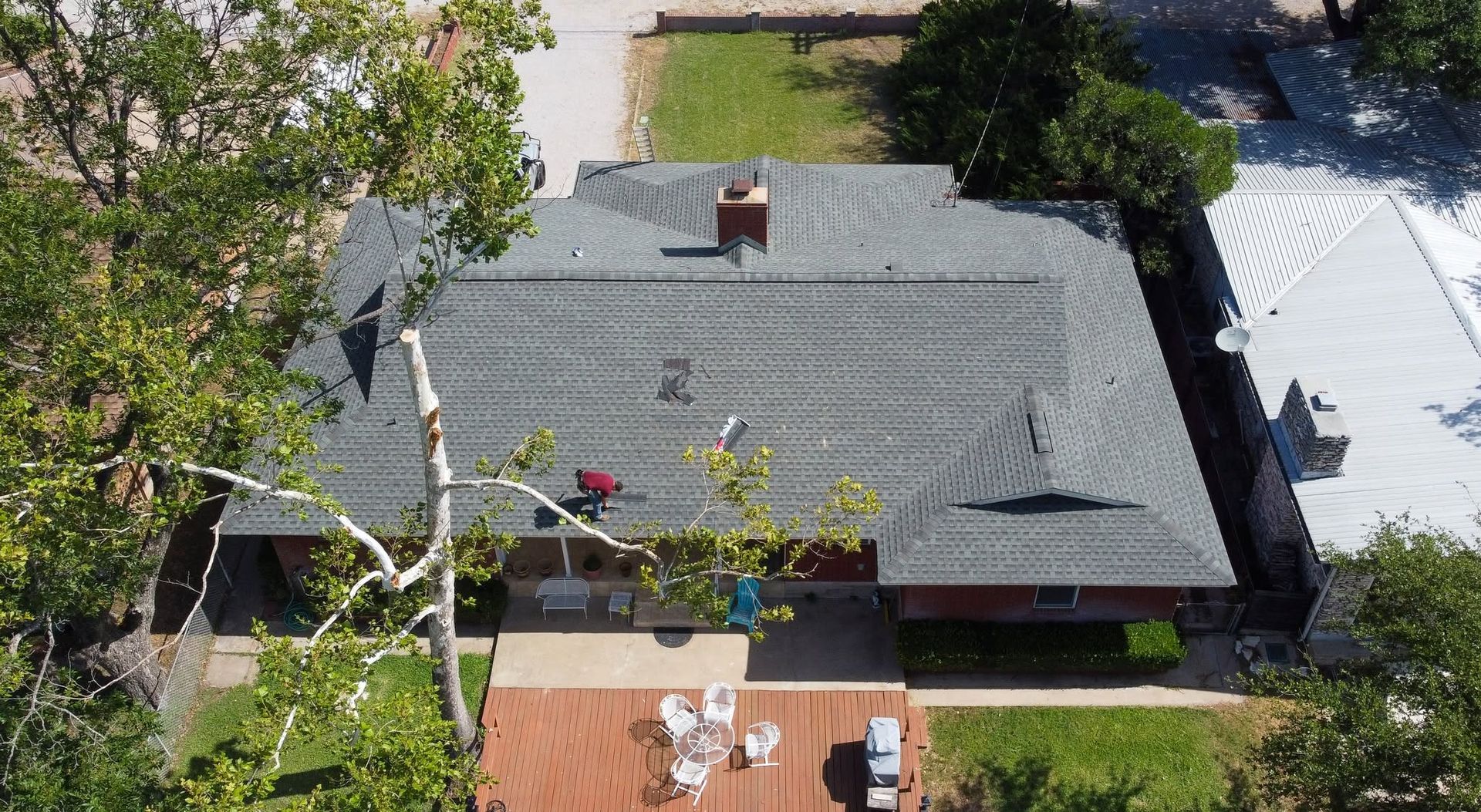 Aerial view of a house with a gray roof, chimney, and backyard patio with outdoor furniture.
