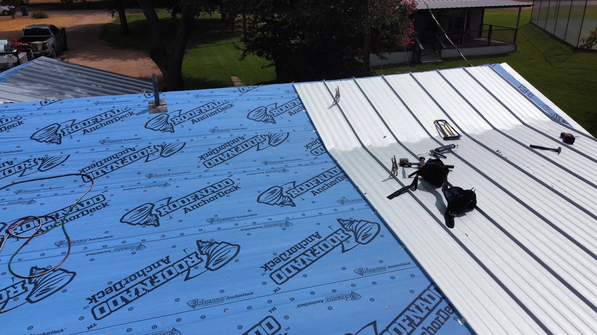Rooftop under repair with blue waterproofing membrane and white panel, tools and debris scattered on top