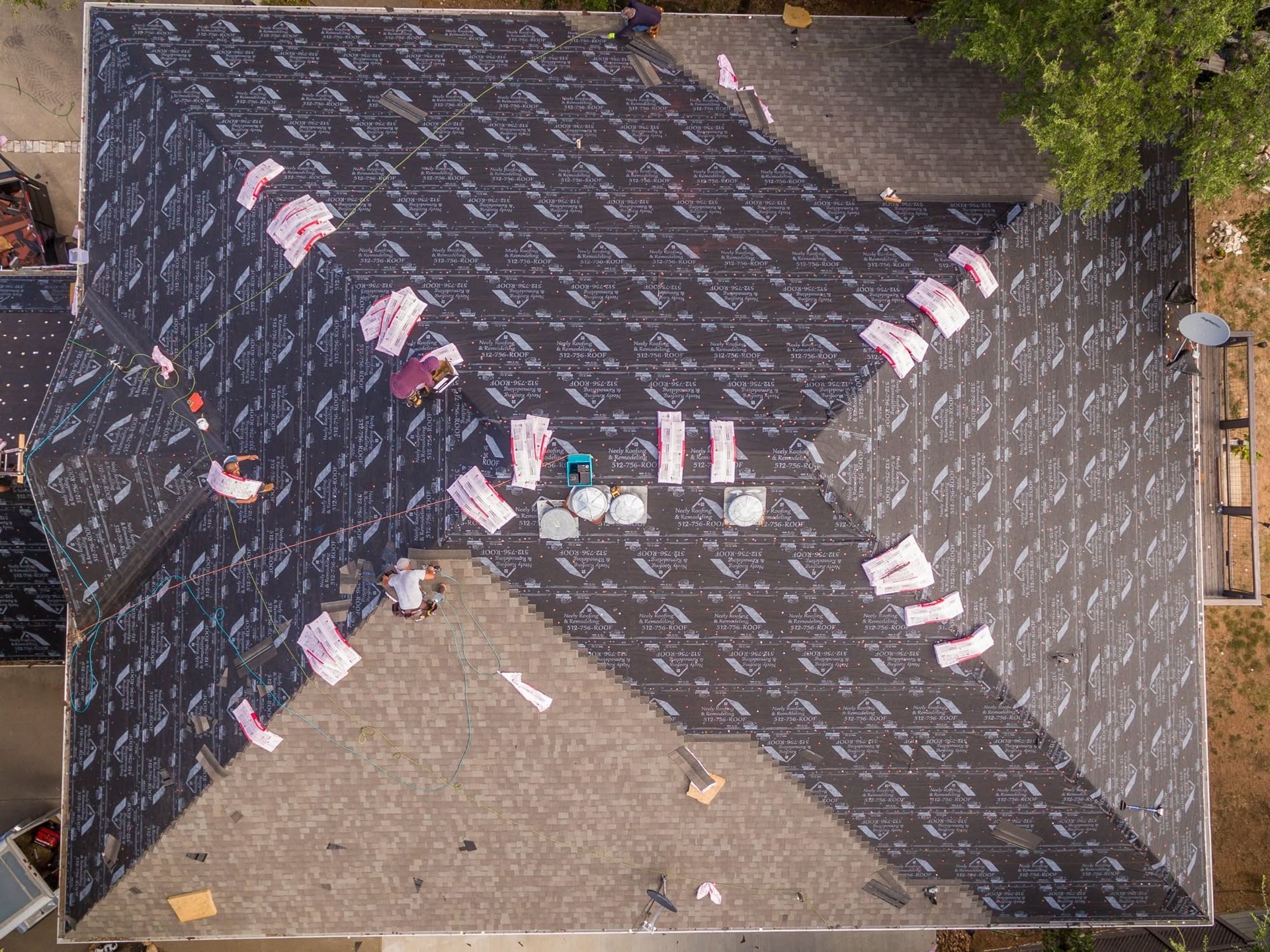 Aerial view of a dark roof with pink-and-white tiles arranged in an X pattern, surrounded by bare ground.