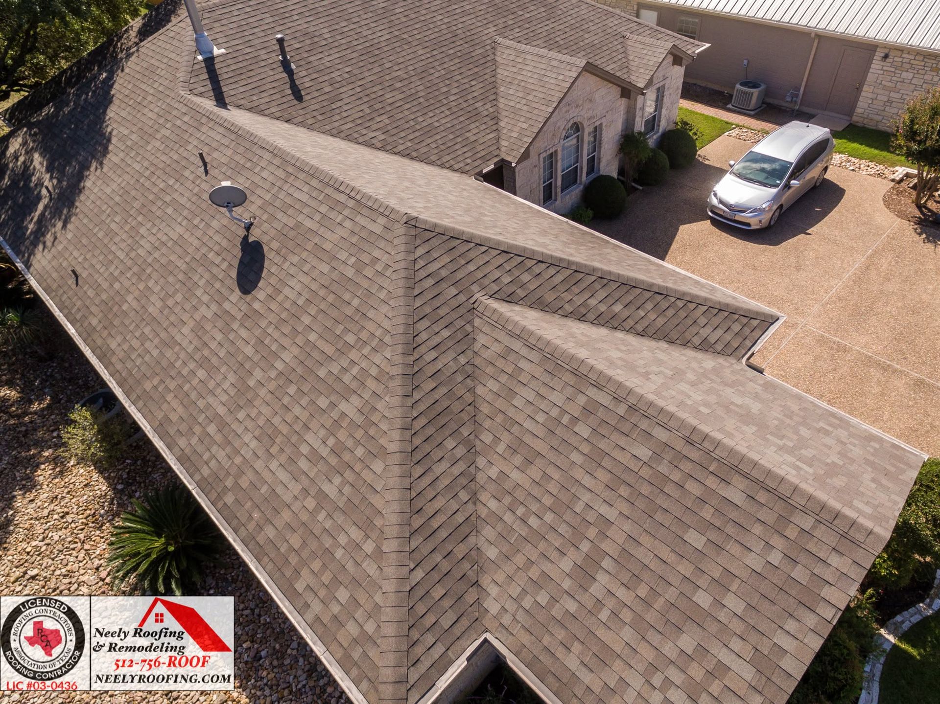 Aerial view of a house roof with dark shingles and a driveway with a parked silver car.