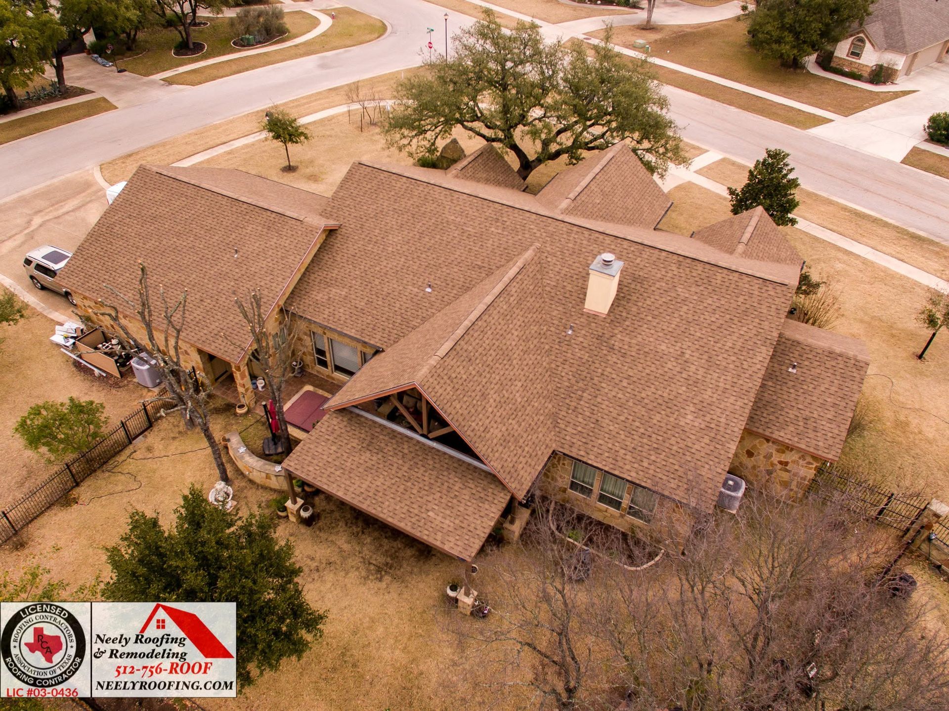 Aerial view of a tan-roofed house with trees and curving roads around it.