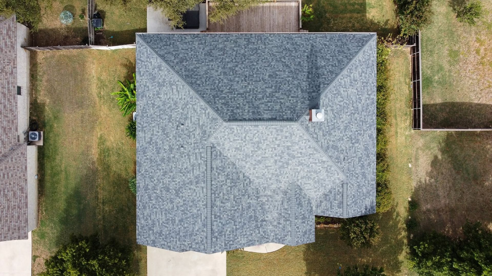 Aerial view of a gray-roofed house with yards and fences on both sides.