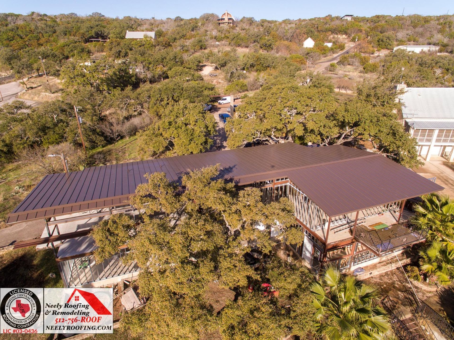 Aerial view of a tree-covered hillside with a long solar-paneled roof and buildings nestled among the trees.