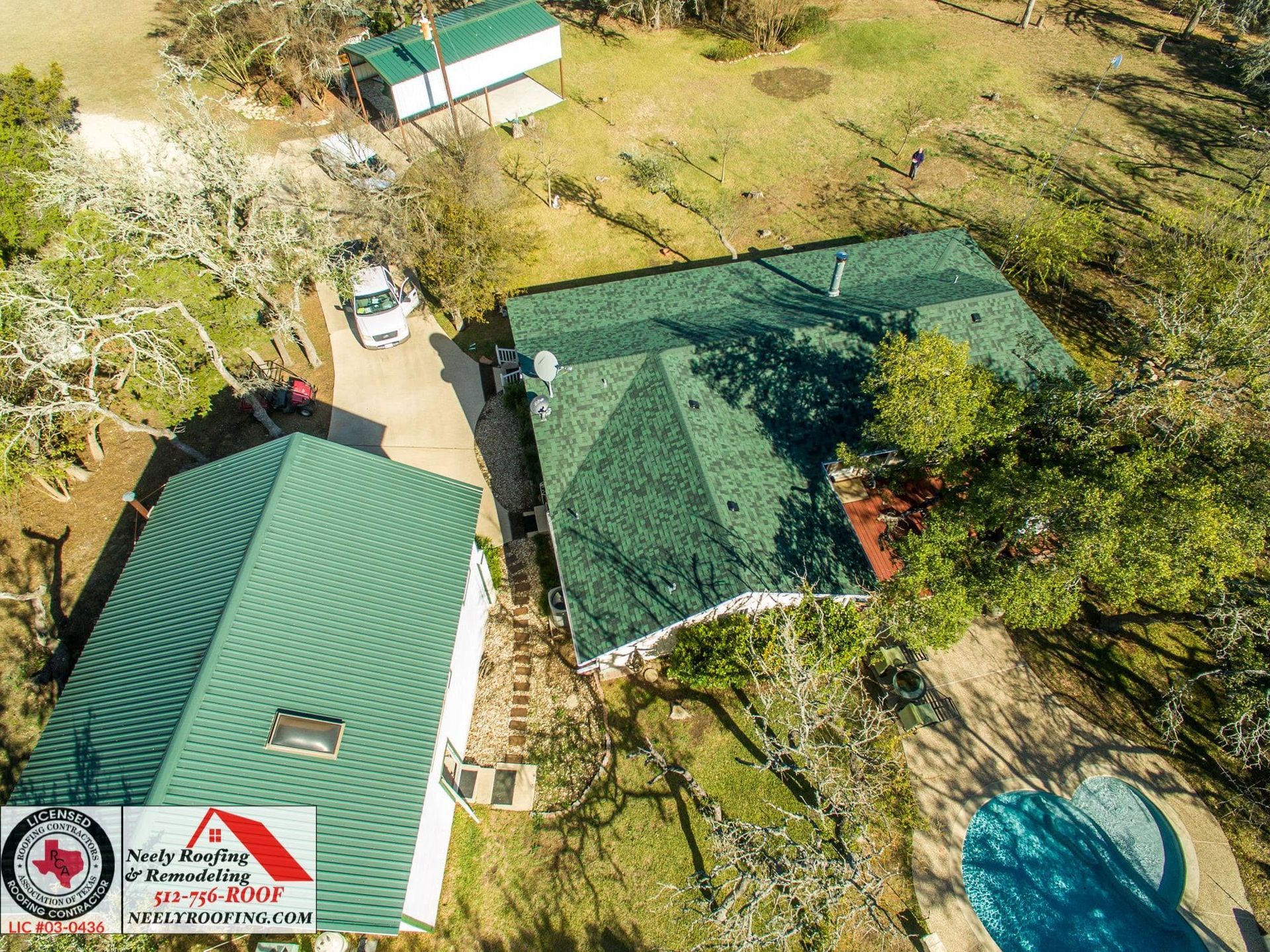 Aerial view of two green-roofed buildings and a driveway surrounded by trees and grass.