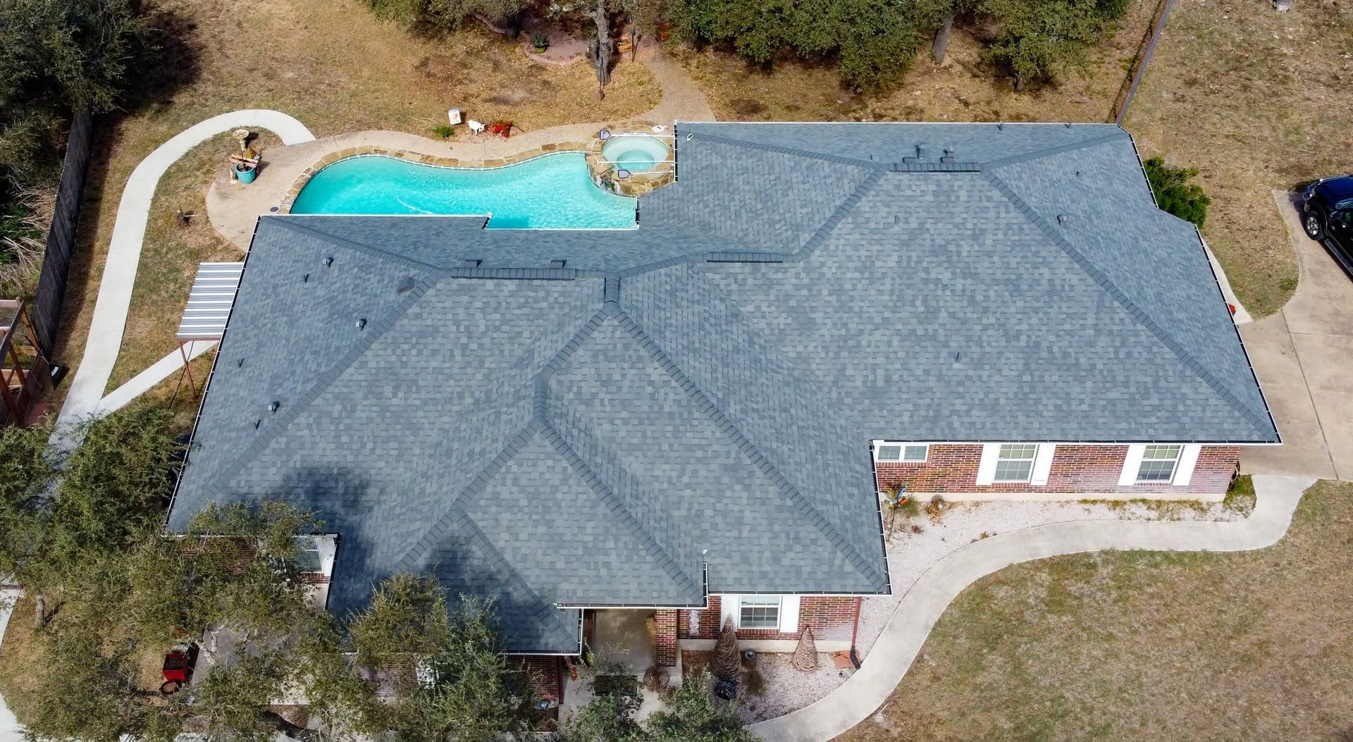 Aerial view of a house with a gray roof, backyard pool, and surrounding yard.