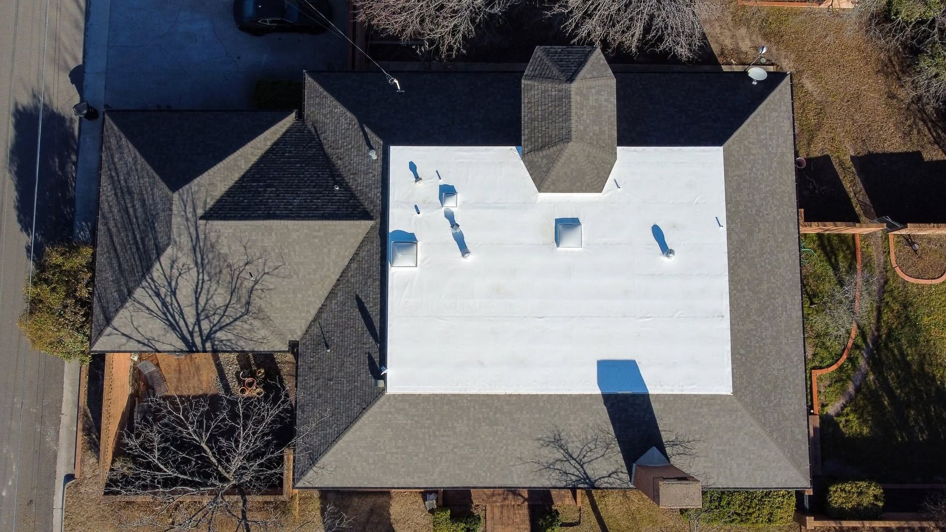 Aerial view of a house roof with a white flat section and a small central chimney.