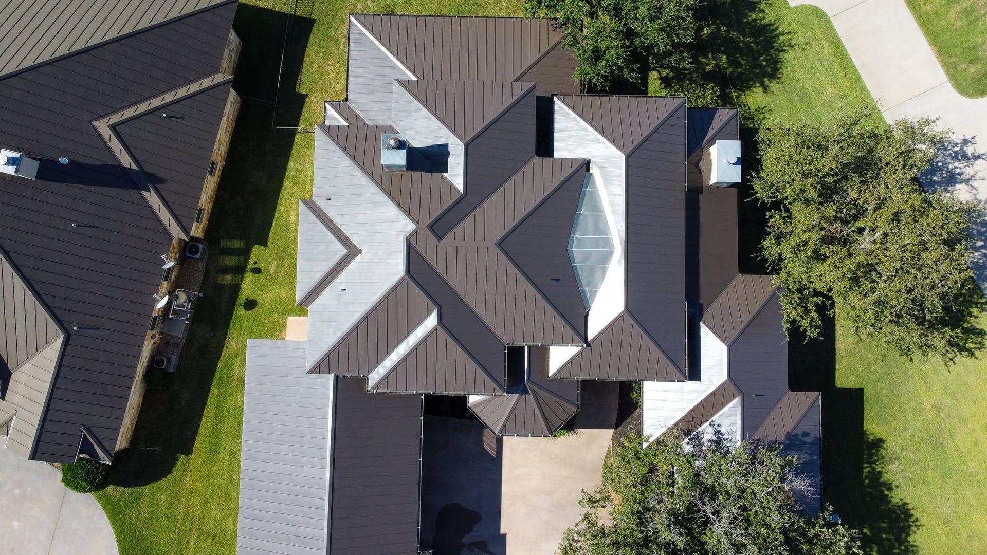 Aerial view of a gray-roofed house with multiple gables, surrounded by lawn and trees.