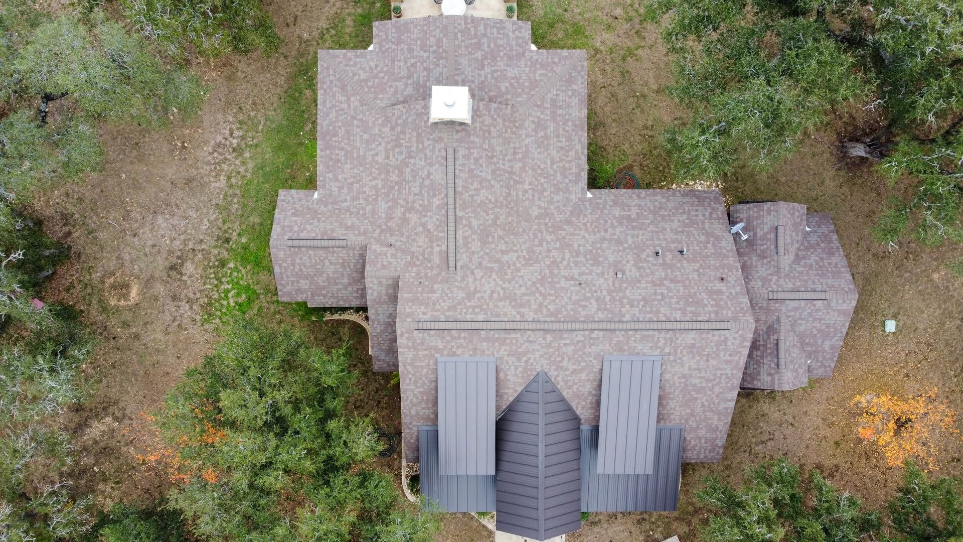 Aerial view of a gray-roofed house with a small front porch, surrounded by greenery.