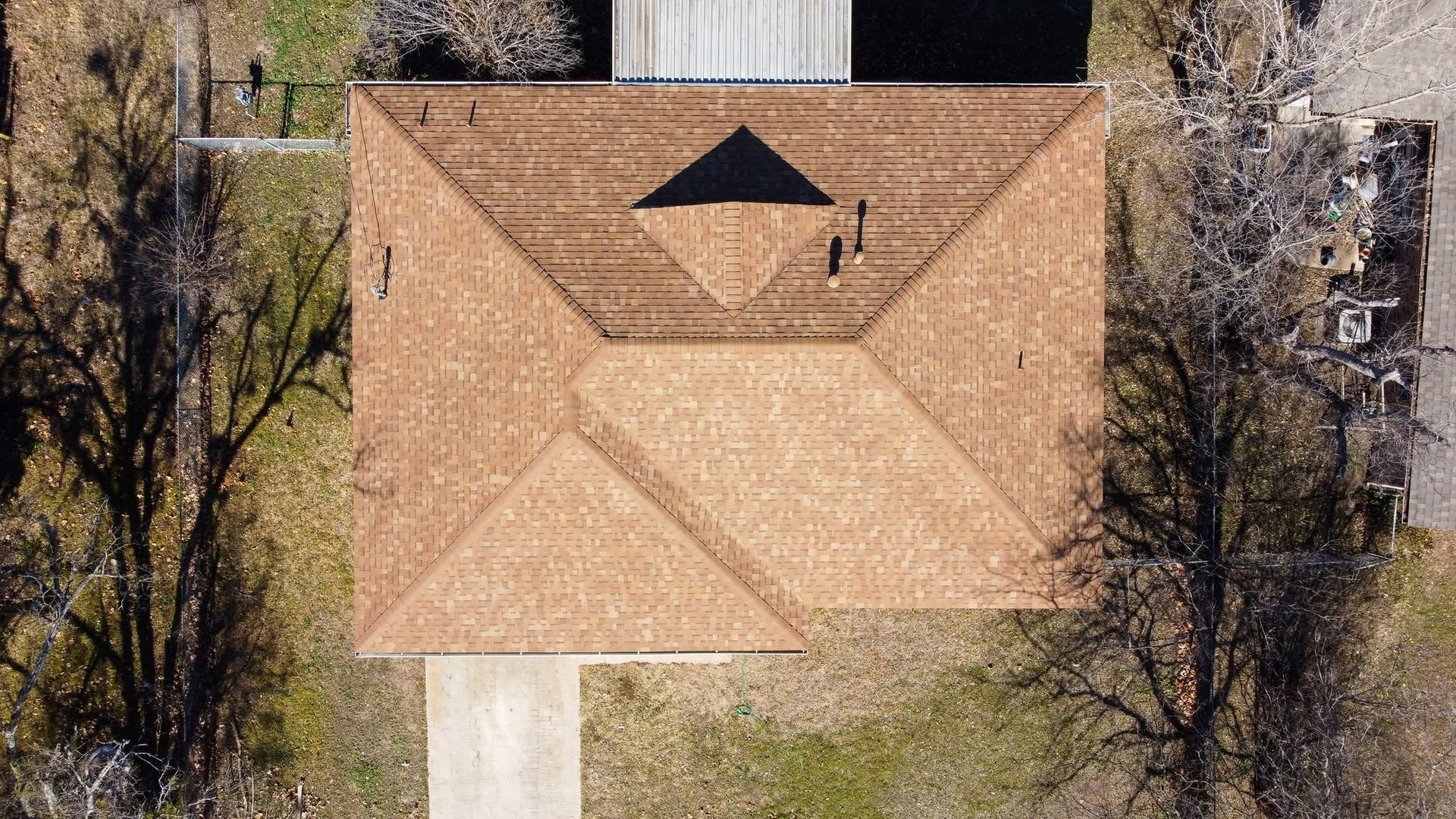 Aerial view of a tan-roofed house surrounded by trees and a driveway
