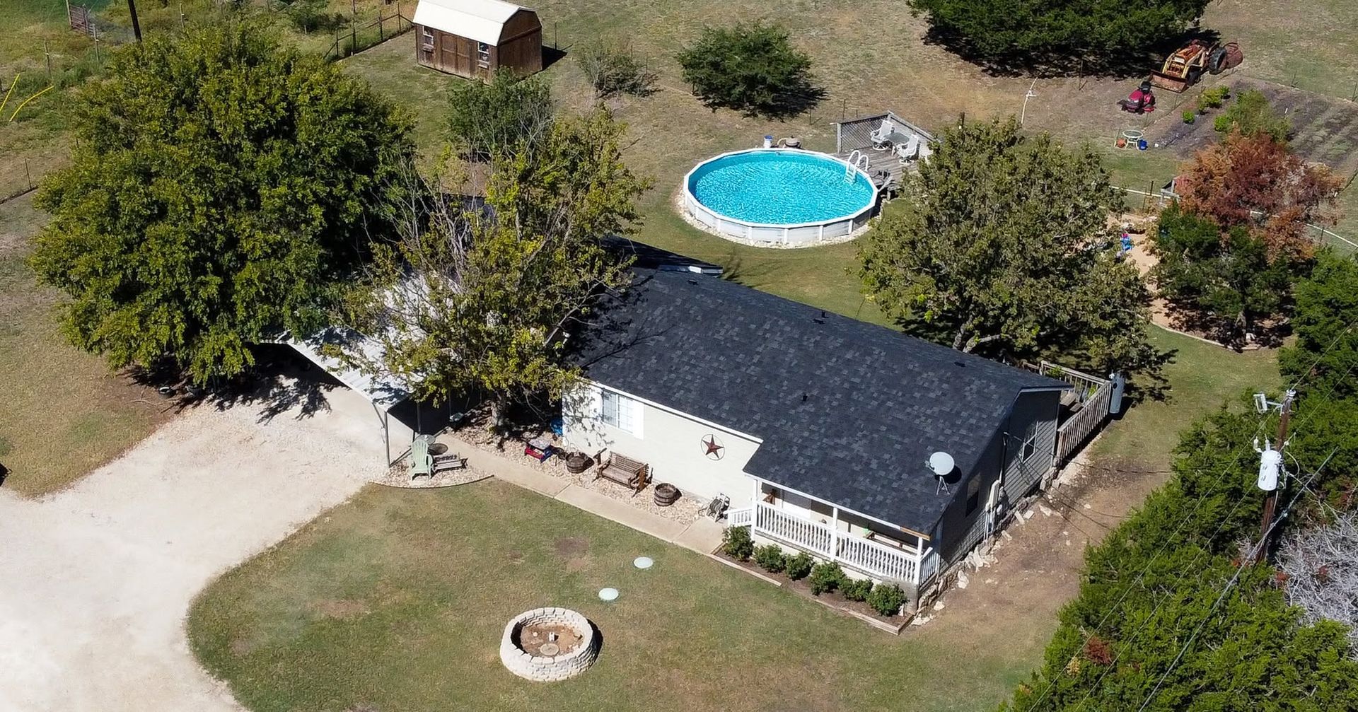 Aerial view of a house with a dark roof, driveway, yard, and a backyard swimming pool.
