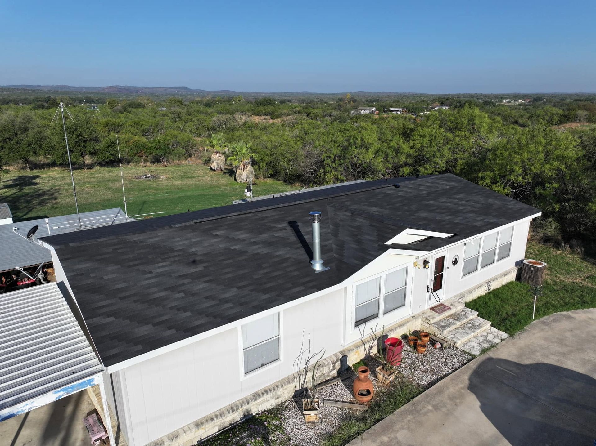 Aerial view of a white house with a black roof, surrounded by trees and open land.