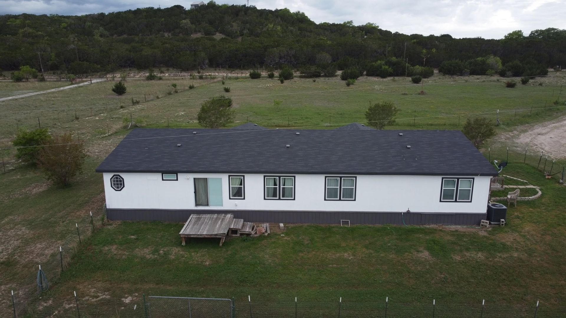 Single-story white house with dark roof in a grassy rural field, seen from above