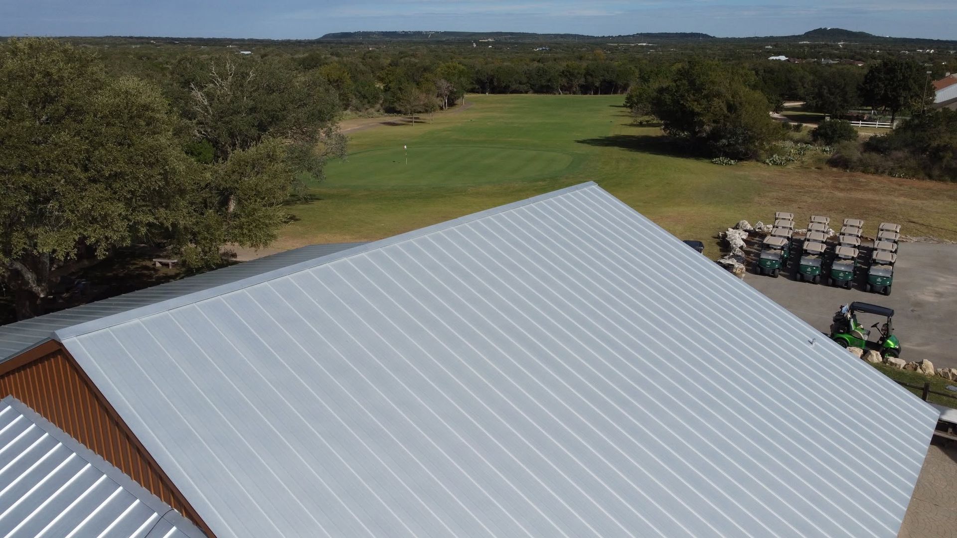 White metal roof in foreground overlooking a green golf course and trees under a clear sky.