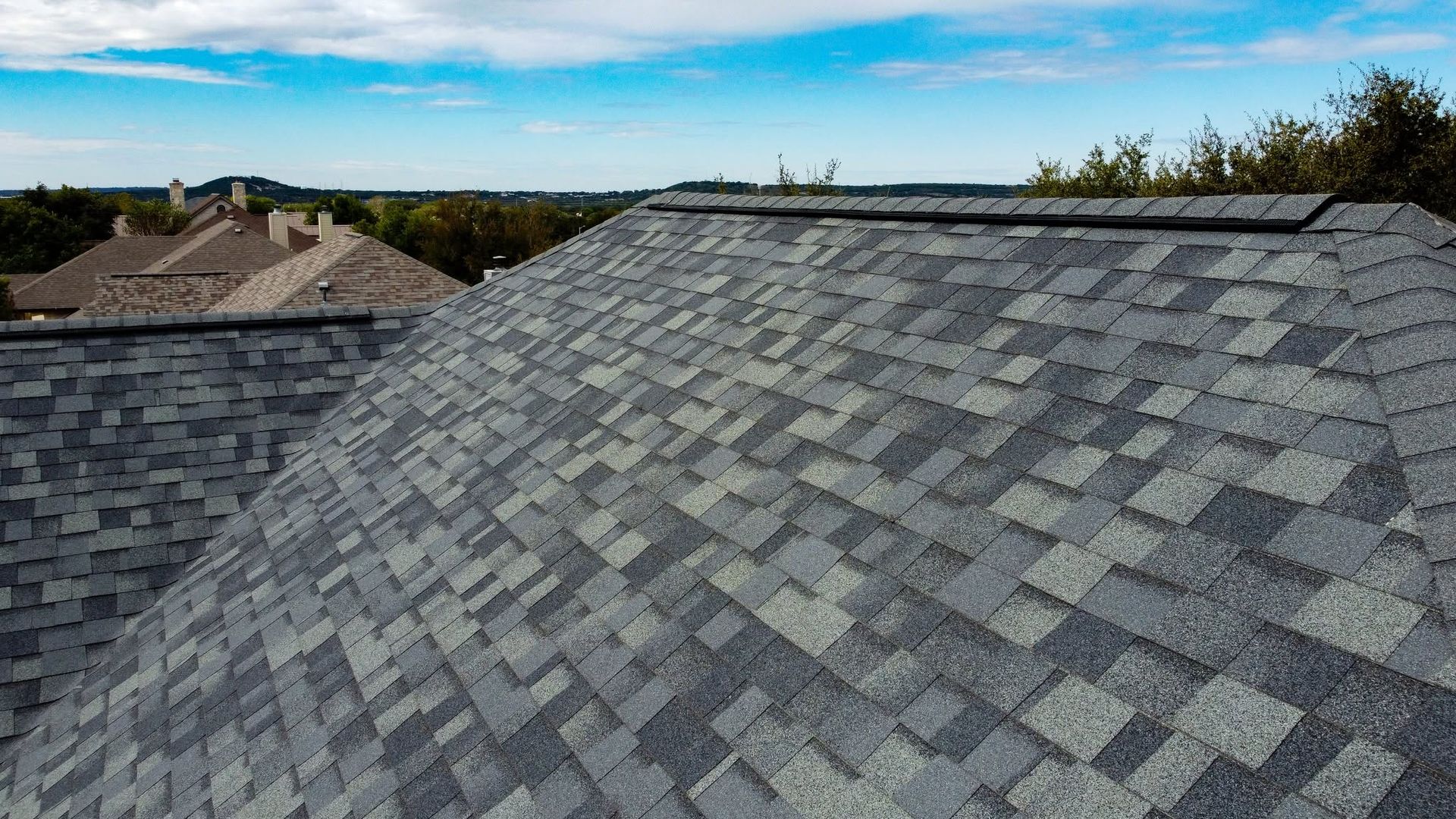 Gray shingle roof under a blue sky, with neighboring rooftops in the background.
