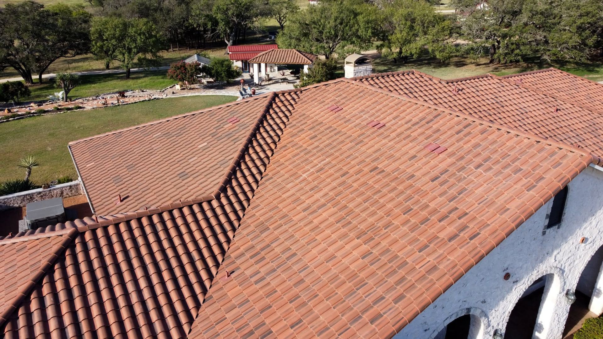 Aerial view of a red-tiled roof on a white building beside a green garden and walkway.