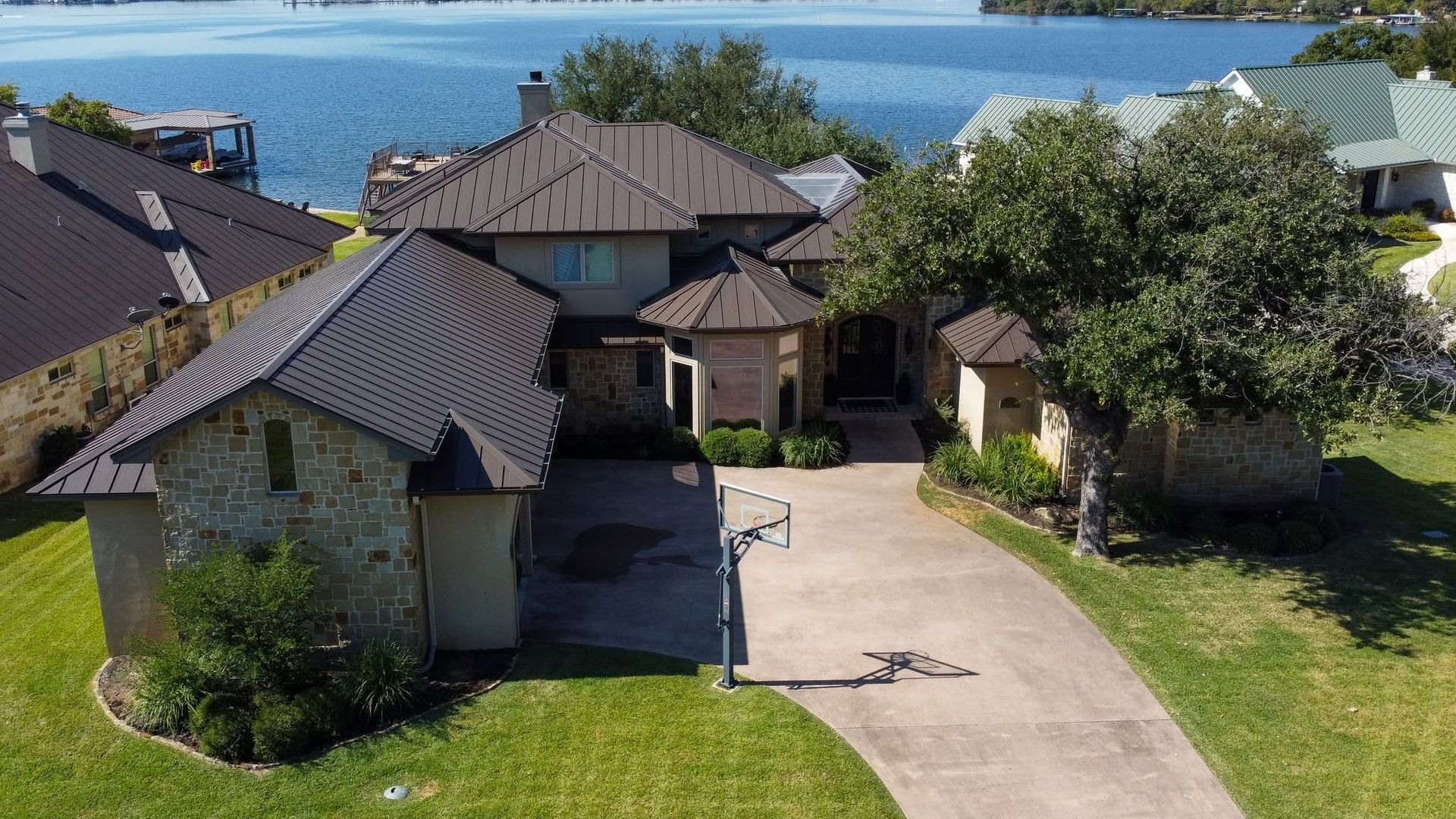 Aerial view of houses with a driveway, green lawns, trees, and a lake in the background