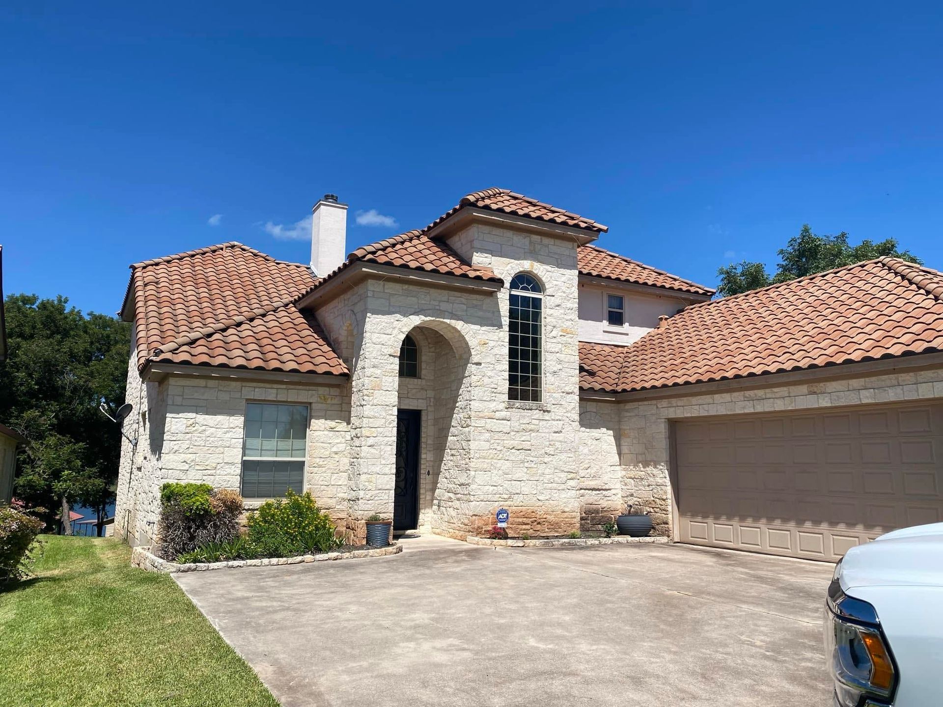 Stone stucco house with red tile roof, arched entry, and large garage under a clear blue sky