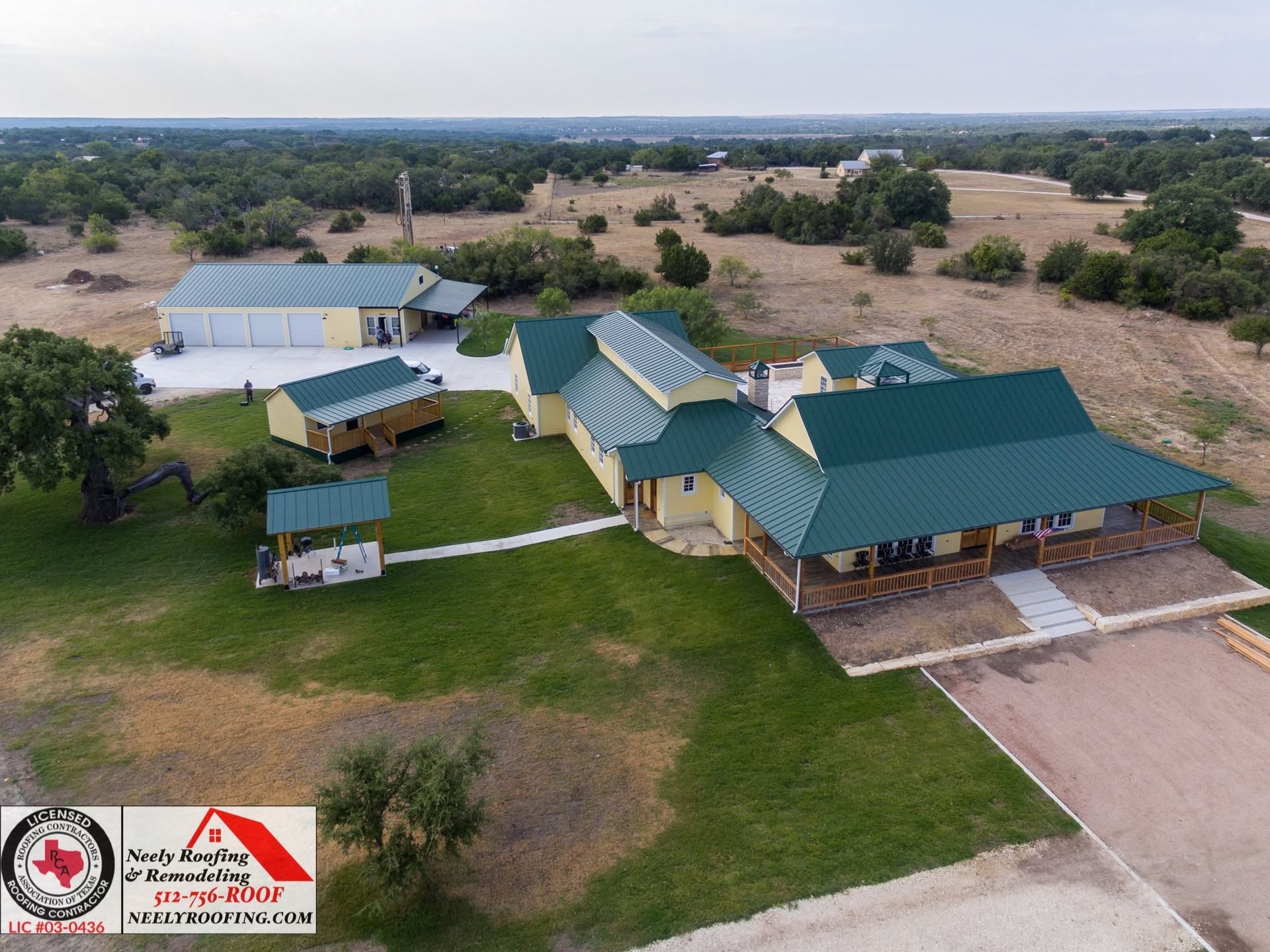 Aerial view of a rural property with green-roofed buildings, lawn, and trees in a dry landscape.
