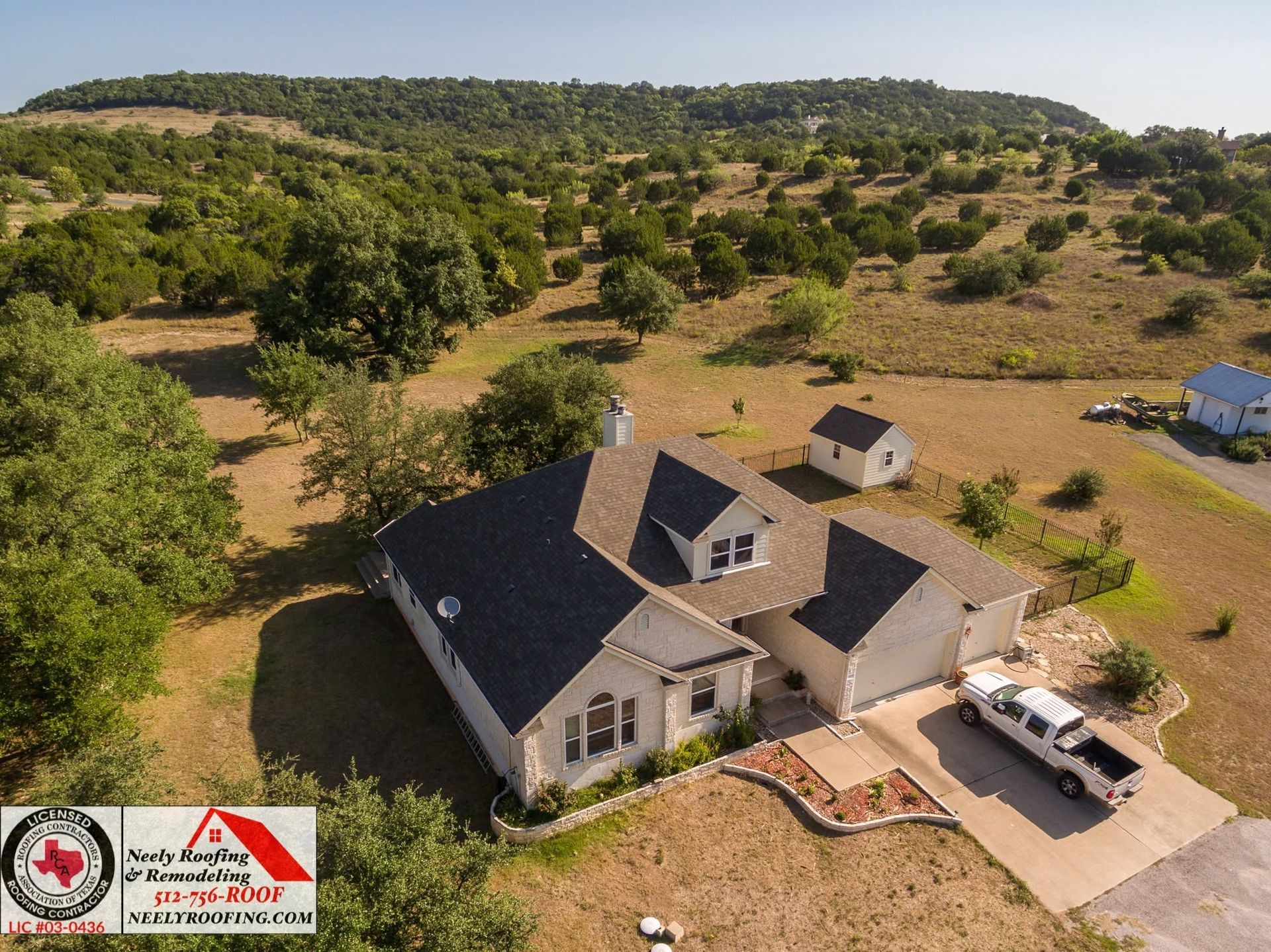 Aerial view of a farmhouse with driveway and parked truck in a rural landscape with scattered trees.