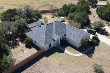 Aerial view of a single-story gray-roofed house surrounded by dry grass and trees.