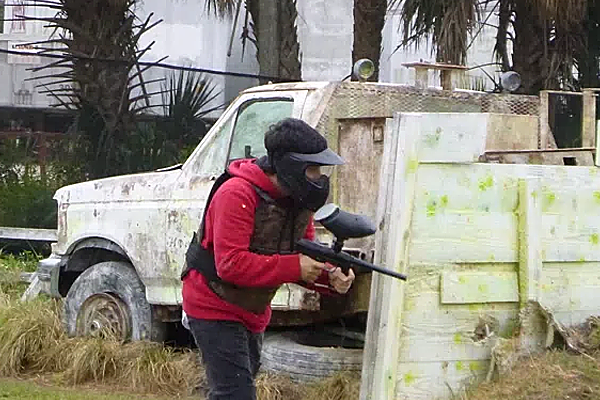 A man is playing paintball in front of a truck.