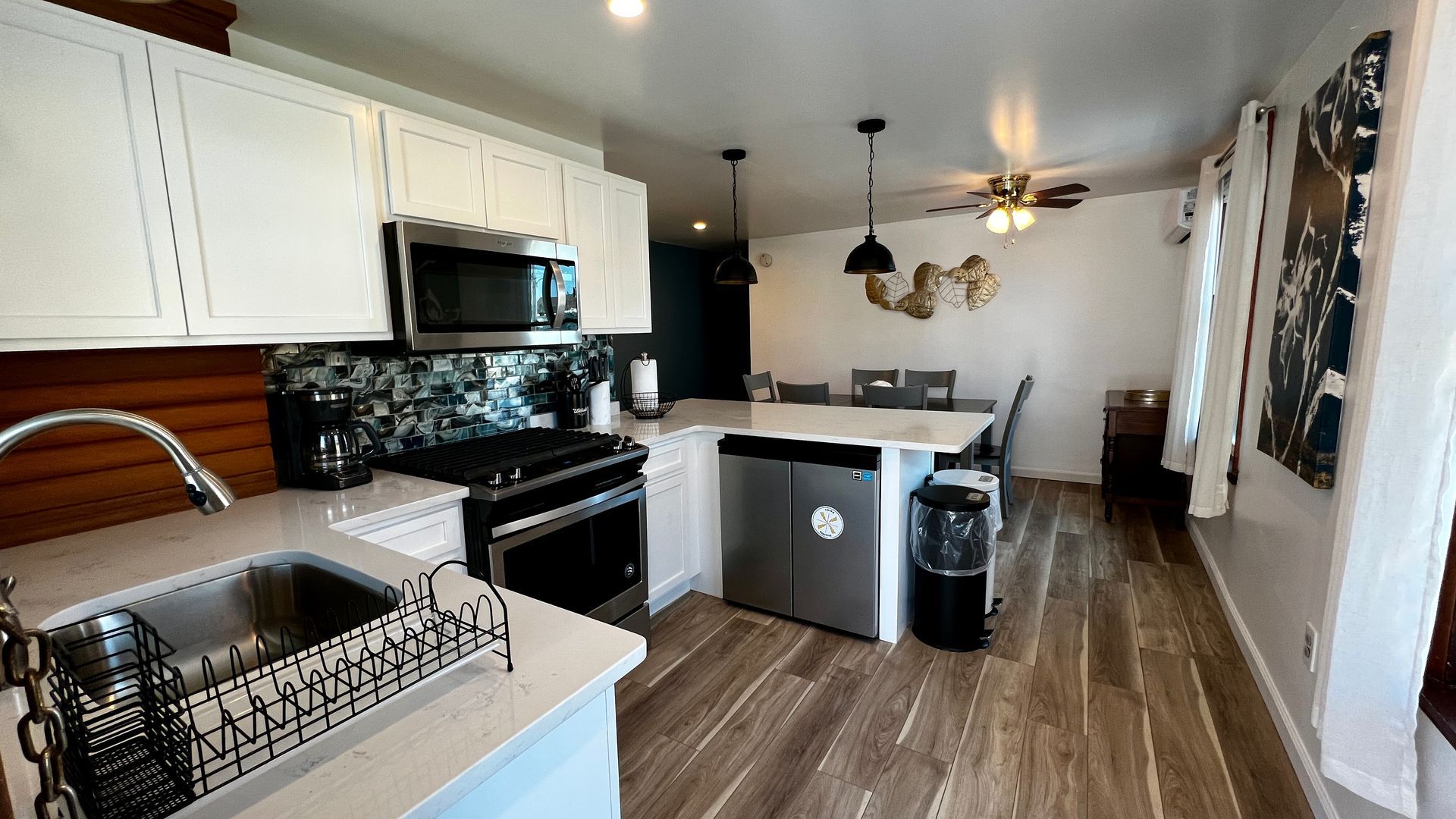 A kitchen with white cabinets , stainless steel appliances , a sink , and a ceiling fan.