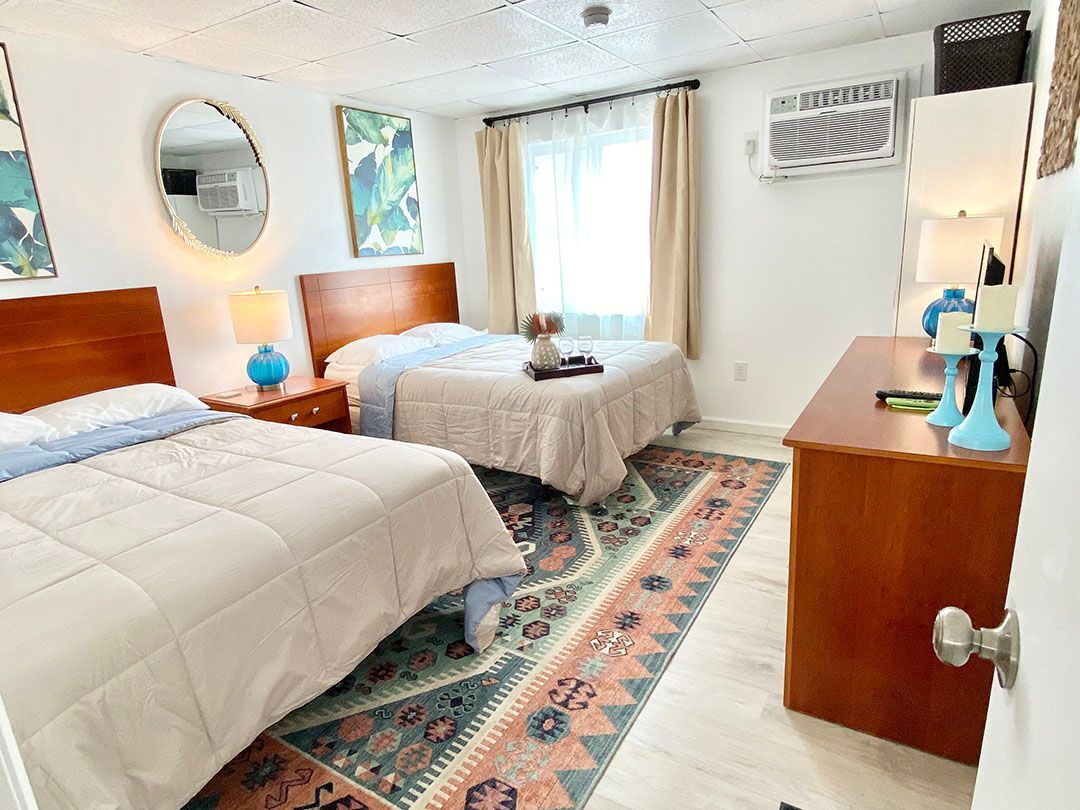 A bedroom with two beds, a dresser, a mirror, and a rug