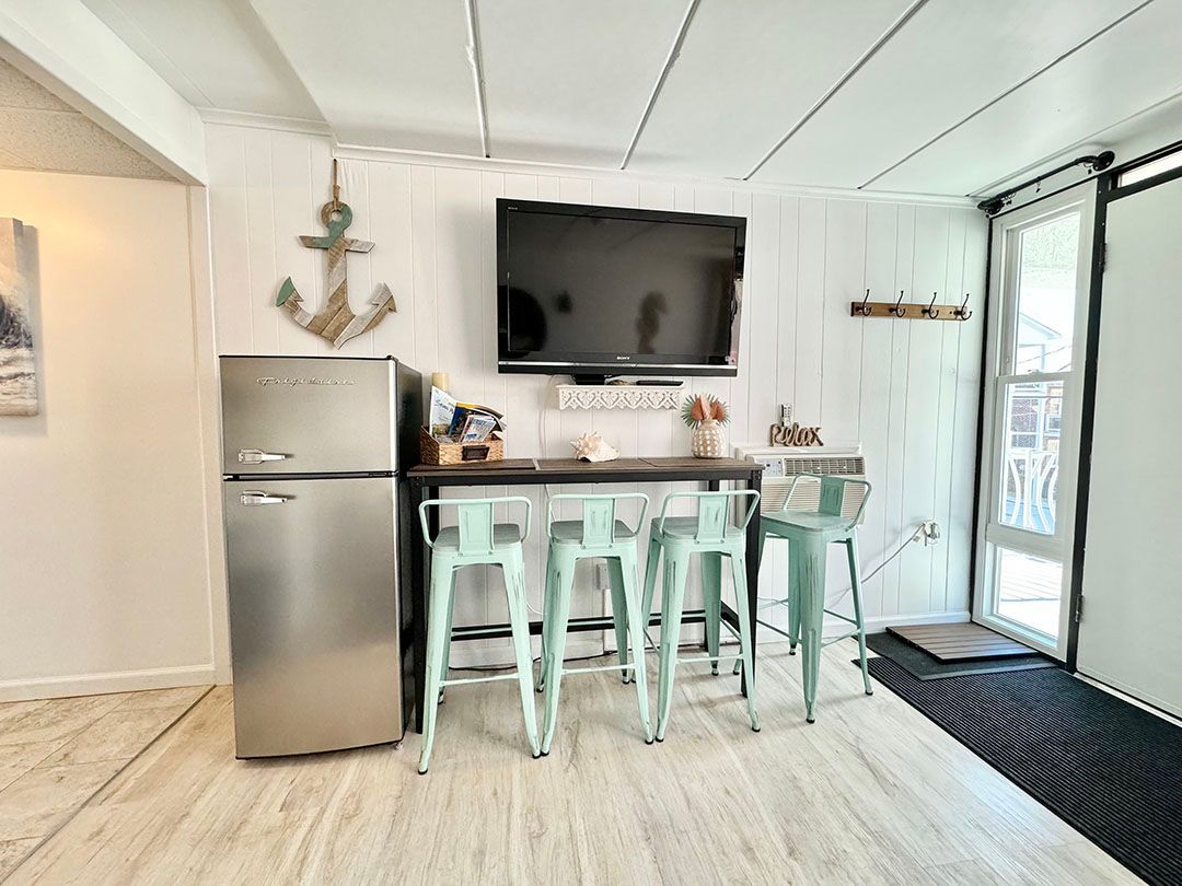 A living room with a refrigerator, stools, and a flat screen tv.
