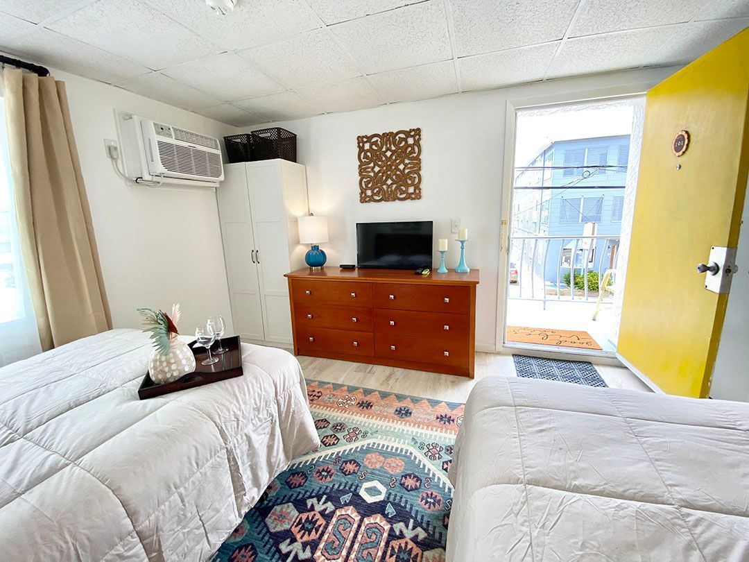 A bedroom with two beds, a dresser, a television, and a yellow door.