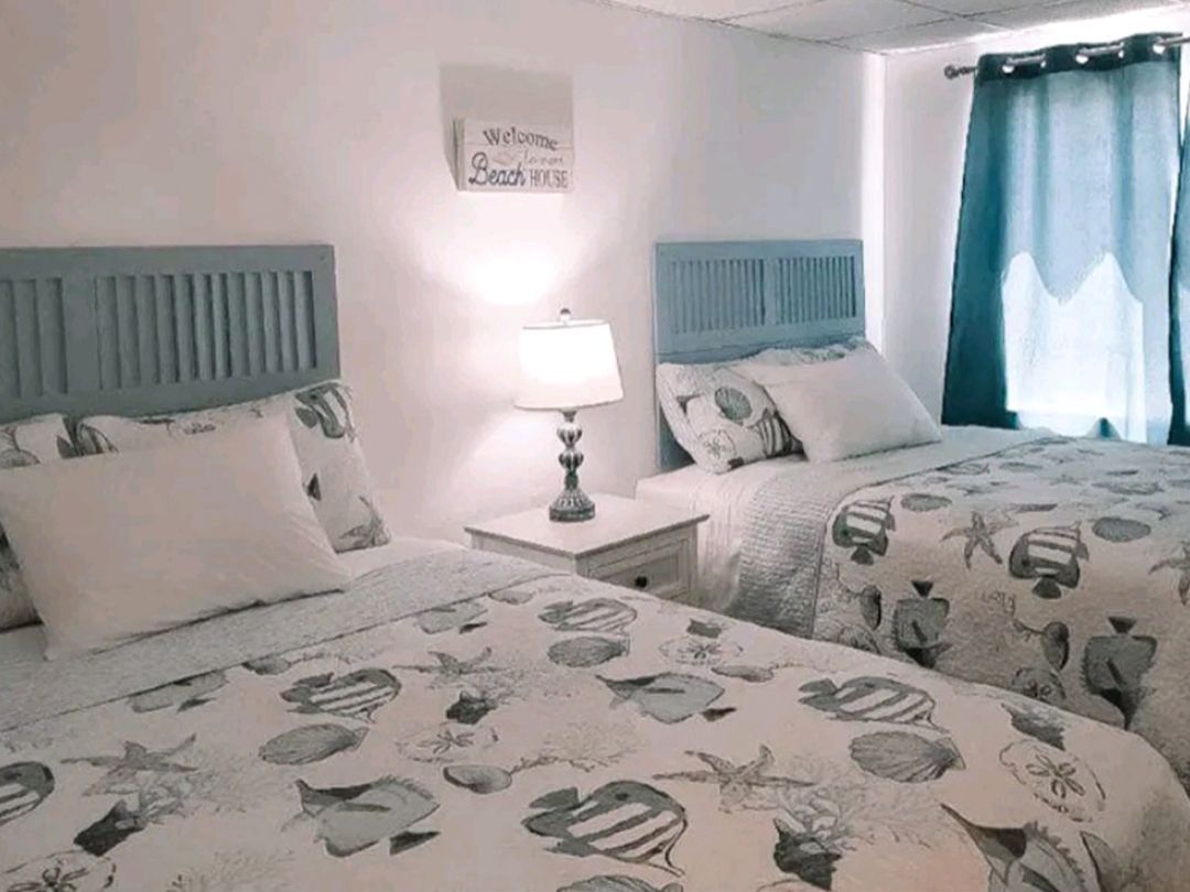 A bedroom with two beds, a nightstand, a lamp, and a window