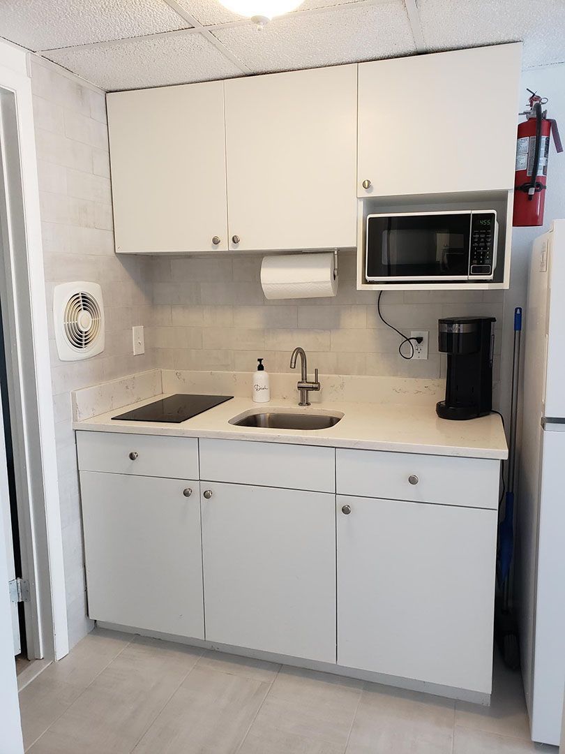 A kitchen with white cabinets a sink a microwave and a refrigerator