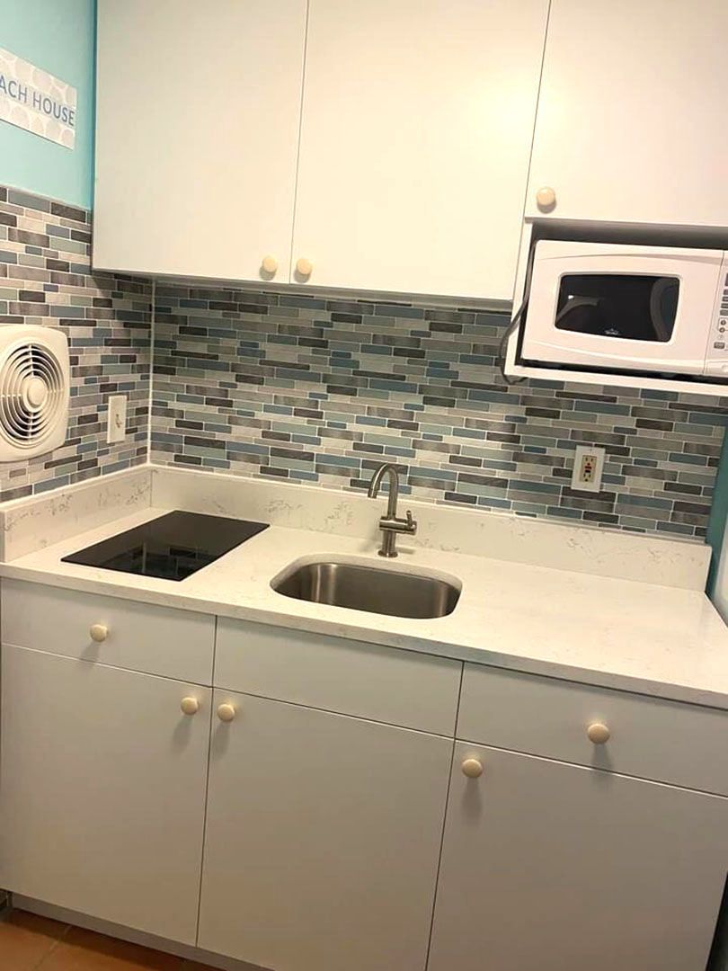 A kitchen with white cabinets, a sink, a microwave, and a fan.